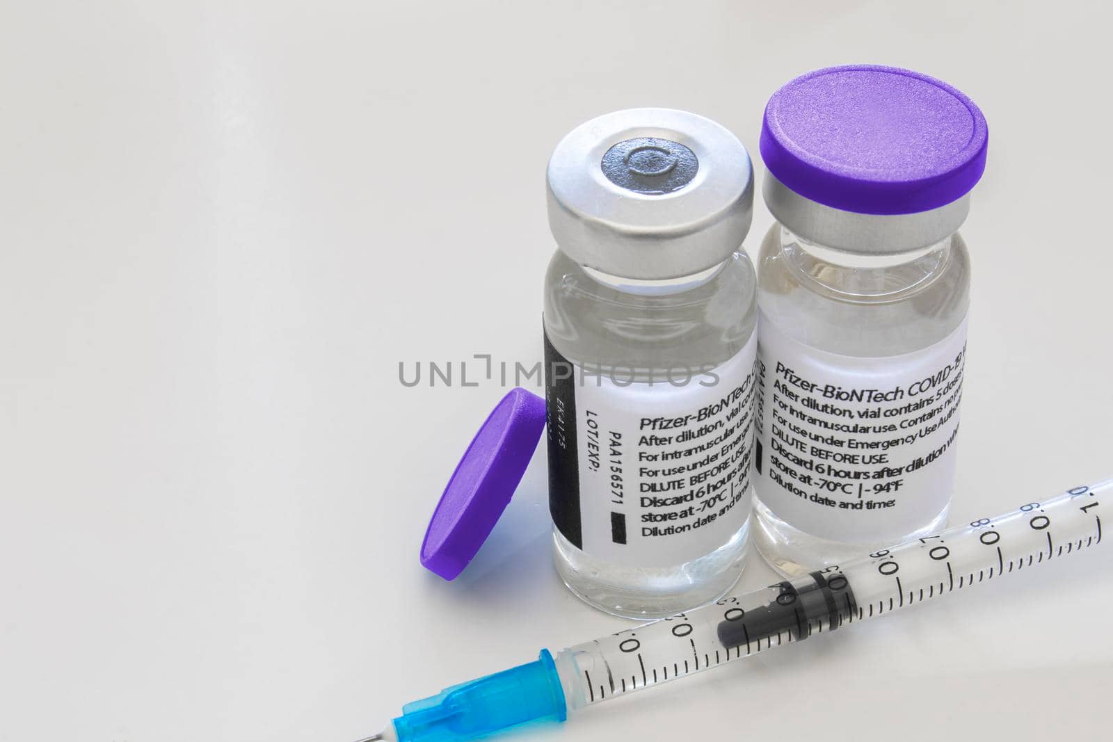 Calgary, Alberta, Canada. April 16, 2021. A couple of Pfizer Covid-19 vaccine vials bottles and an injection syringe on a clear table.