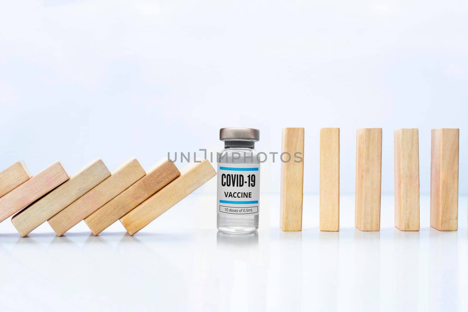 Wooden pieces domino effect stopping fall with a Covid-19 vial vaccine, next to stand wooden pieces Concept: Covid-19 vaccine stopping crisis and risk, protection concept. by oasisamuel