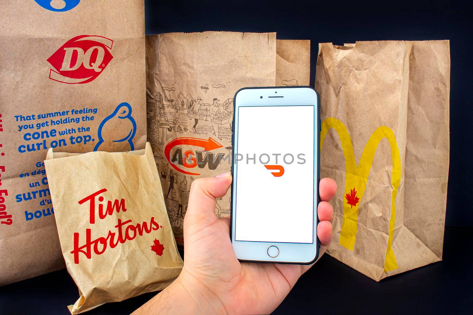 Calgary, Alberta. Canada. April 24, 2020: A person holding an iPhone Plus with the Door Dash application open with delivered food bags from Tim Hourtons, A&W, McDonals and DQ