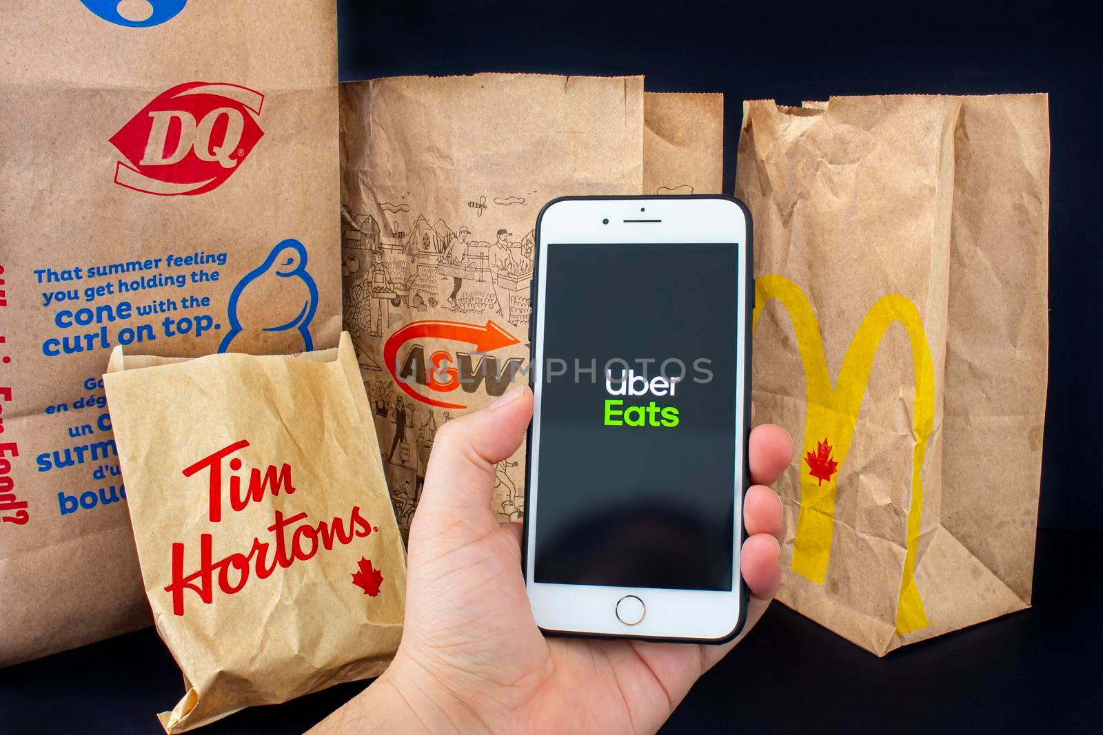 Calgary, Alberta. Canada. April 24, 2020: A person holding an iPhone Plus with the Uber Eats application open with delivered food bags from Tim Hourtons, A&W, McDonals and DQ