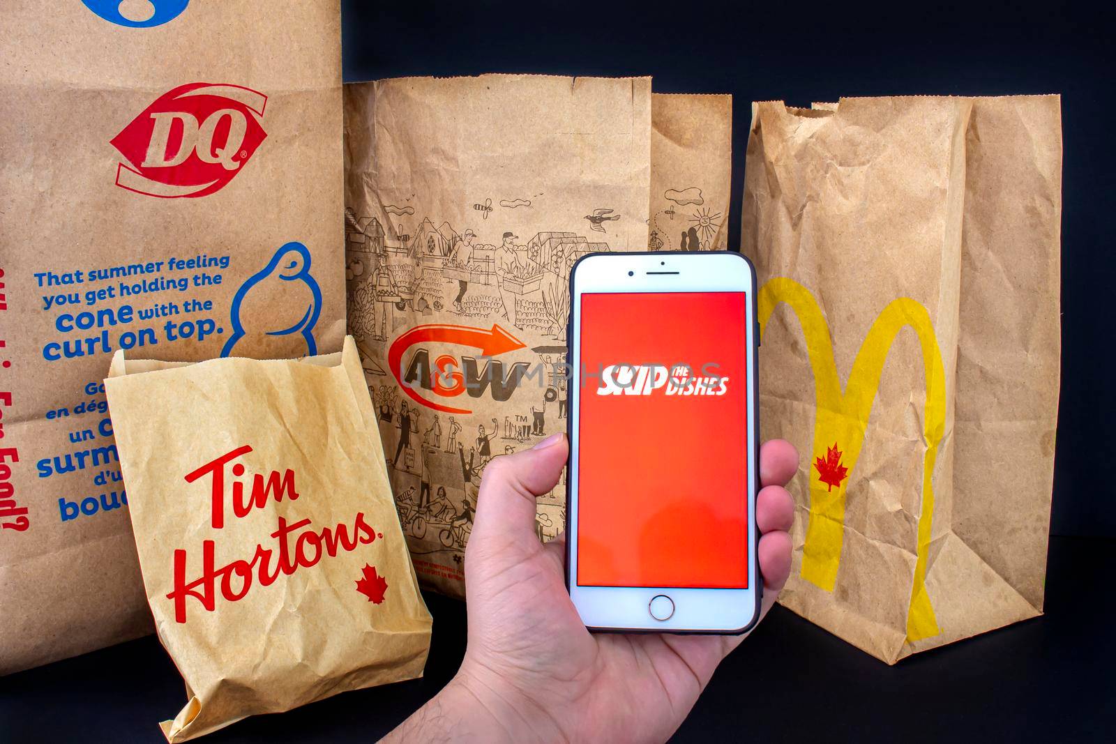 Calgary, Alberta. Canada. April 24, 2020: A person holding an iPhone Plus with the Skip the dishes application open with delivered food bags from Tim Hourtons, A&W, McDonals and DQ