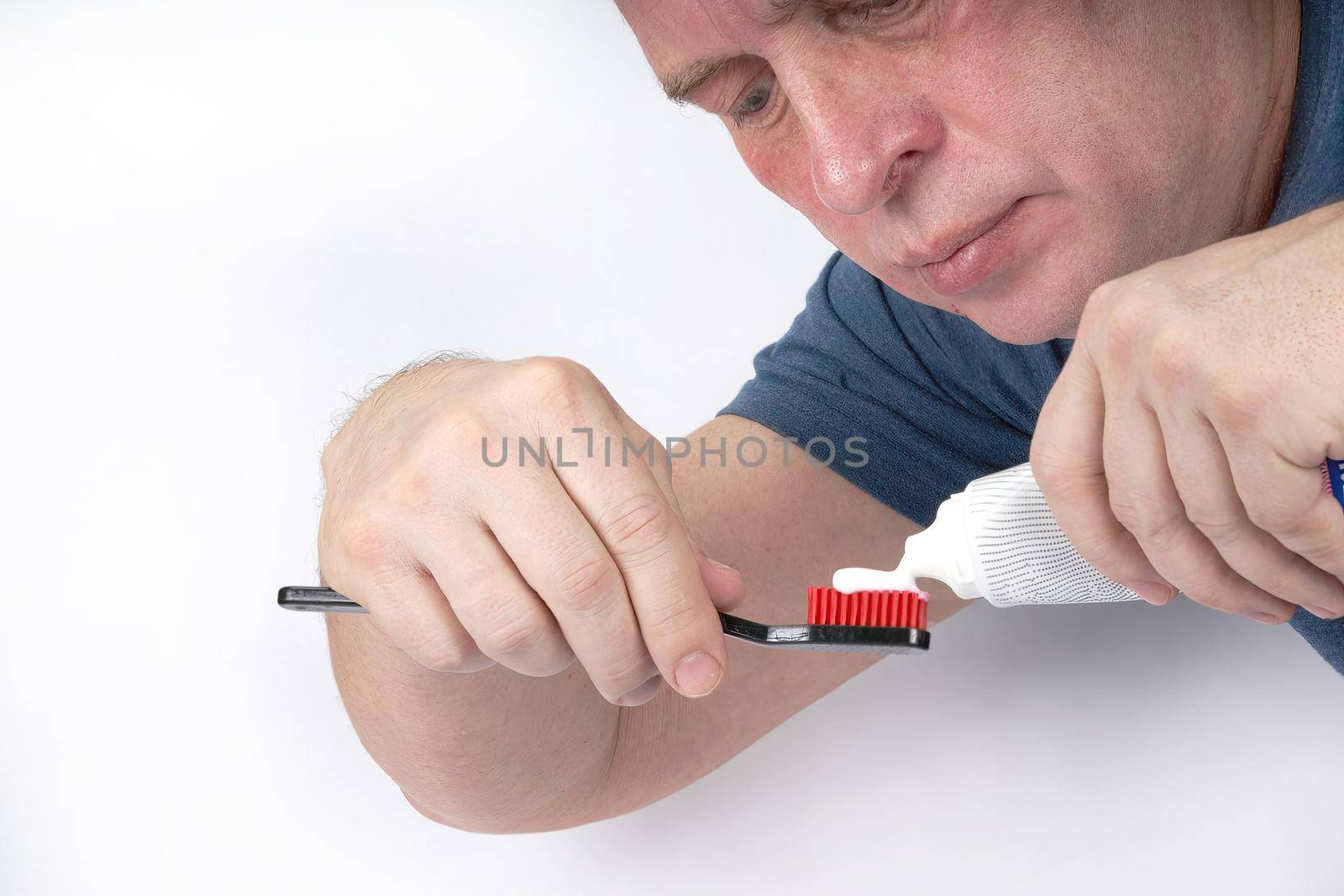 Man squeezes toothpaste onto black toothbrush with red shield on white background
