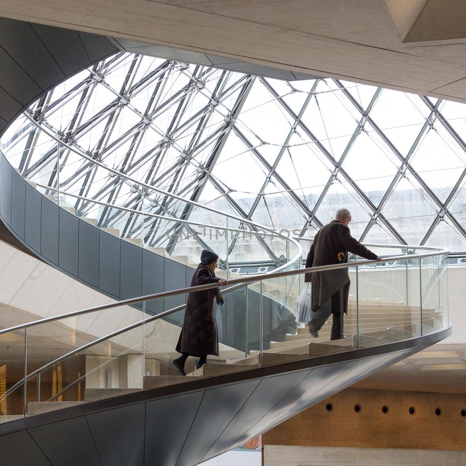 Paris, France - February 20 2014: Man and woman climb spiral staircase at The Louvre Paris by LeoniekvanderVliet