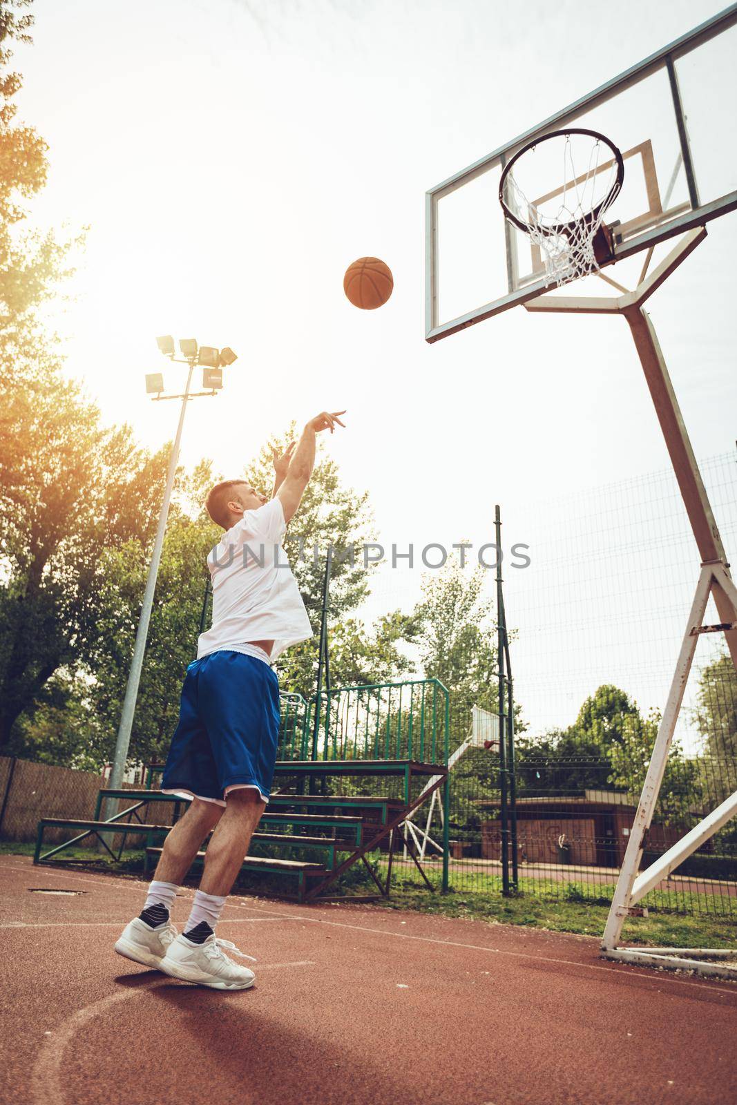 Young street basketball player showing his skills on court. He throw dunk.
