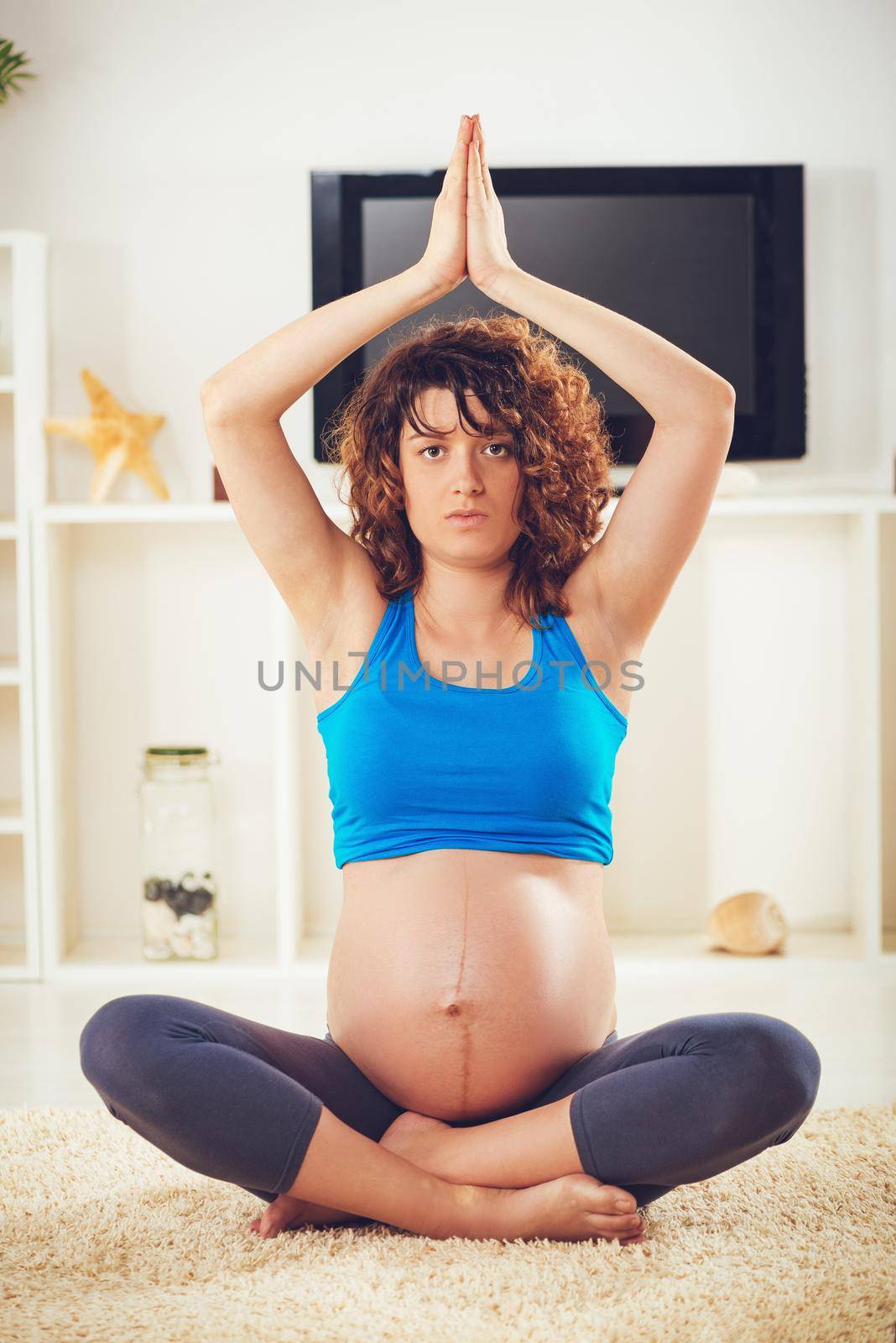 Beautiful young pregnant woman doing yoga exercise at the home. Looking at camera.