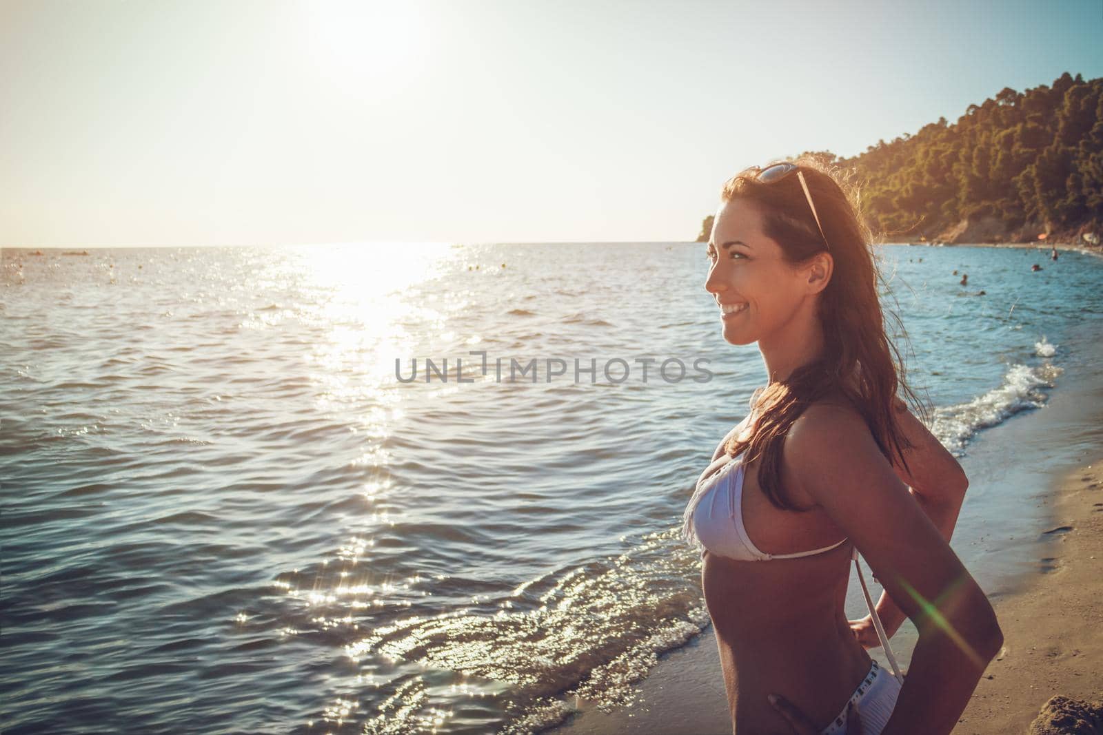 Beautiful young woman relaxing on the beach. She is posing and pensive looking away with smile on her face. 