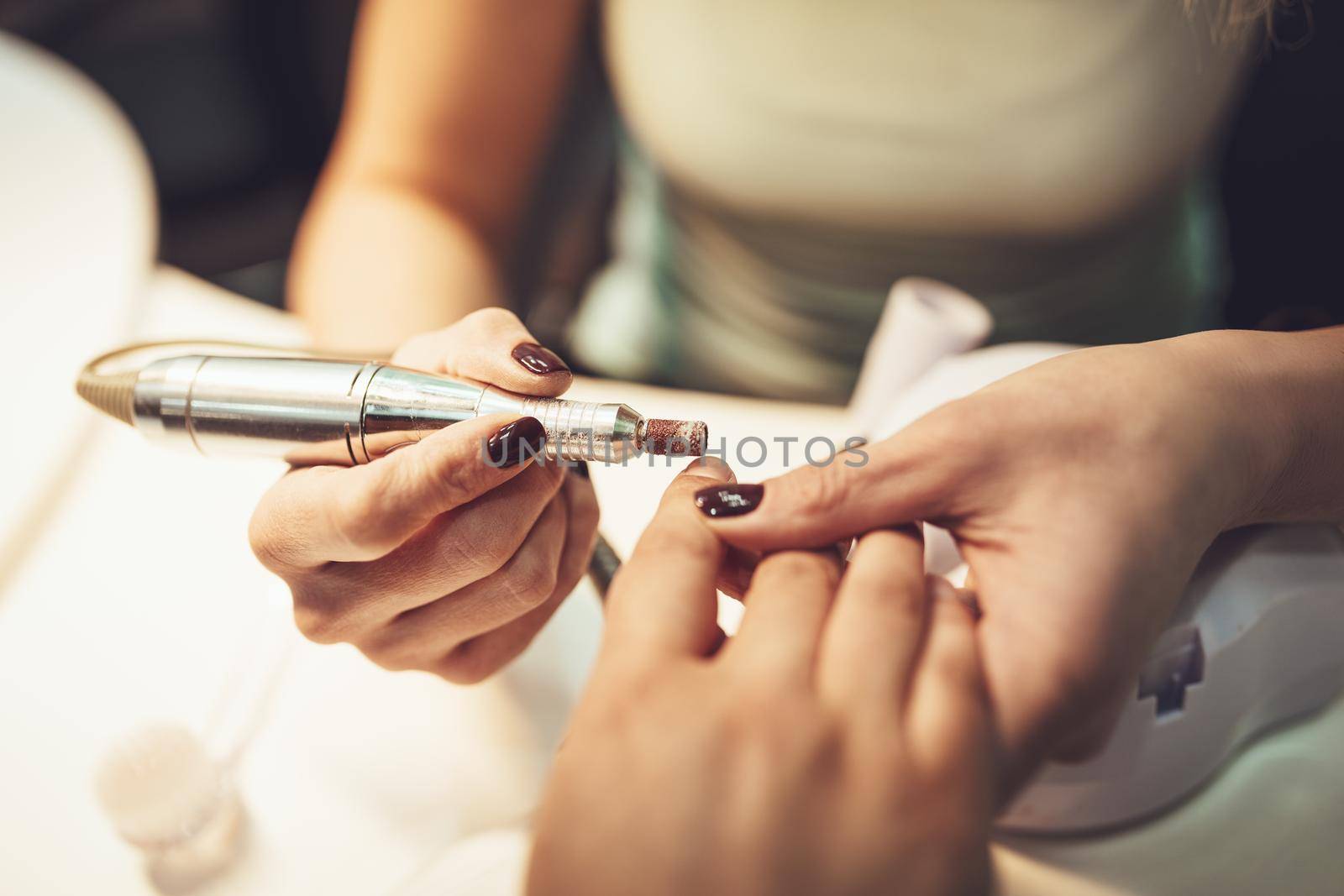 Close-up of a beautician polishing female clients nails with nail file at the beauty salon.