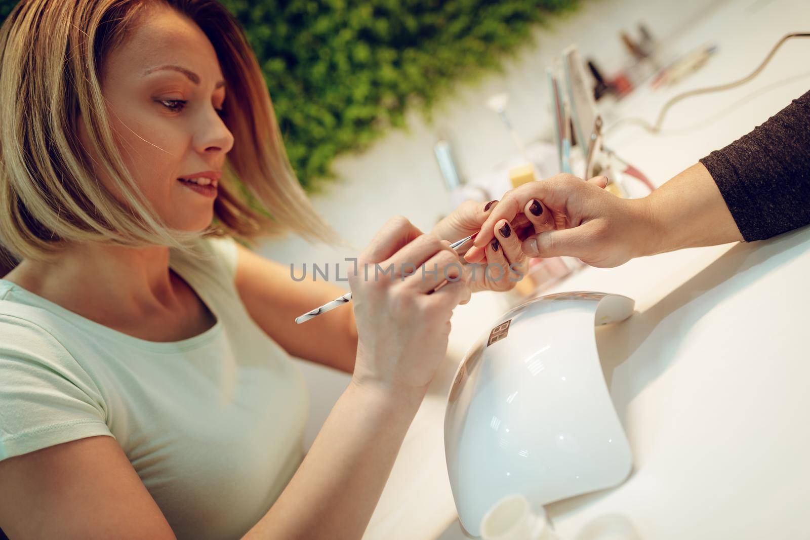 Happy beautician paint the nails of female clients at the beauty salon.