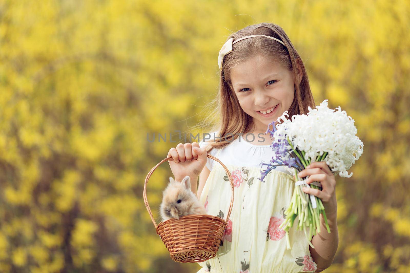 Beautiful smiling little girl holding little basket with cute Easter bunny and bouquet of flowers hyacinth in spring holidays. Looking at camera.