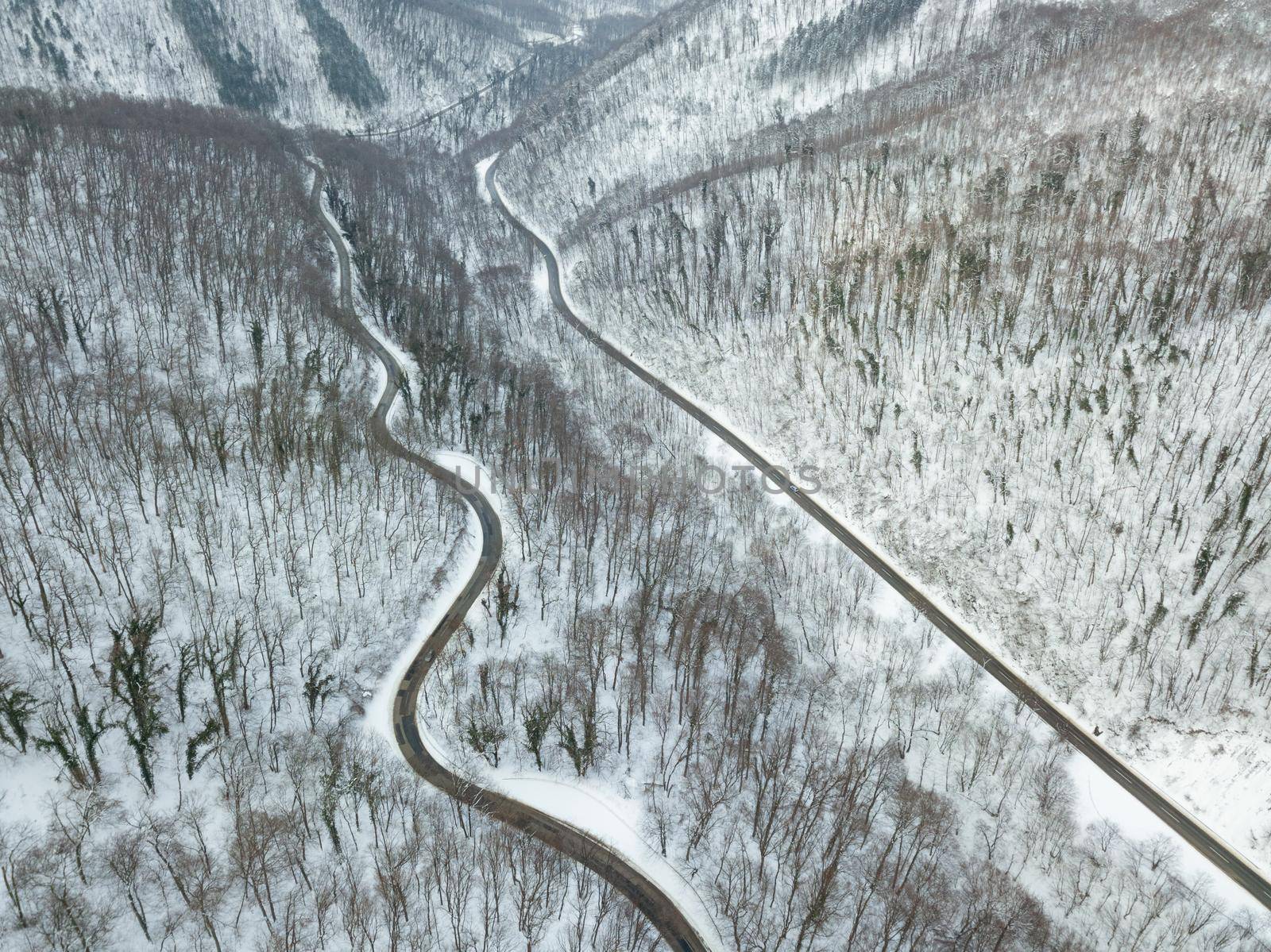 Drone aerial top view of a road going through forest with snow.