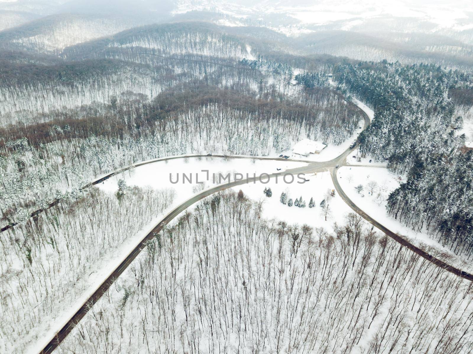 Drone aerial top view of a road going through forest with snow.