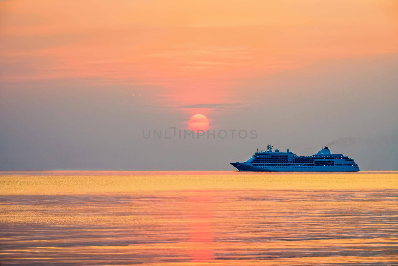 Travel by Cruise ship in the ocean, large luxury passenger boat is sailing on the bright sea, red sun in the colorful sky is yellow, orange, beautiful nature landscape at sunset or sunrise background