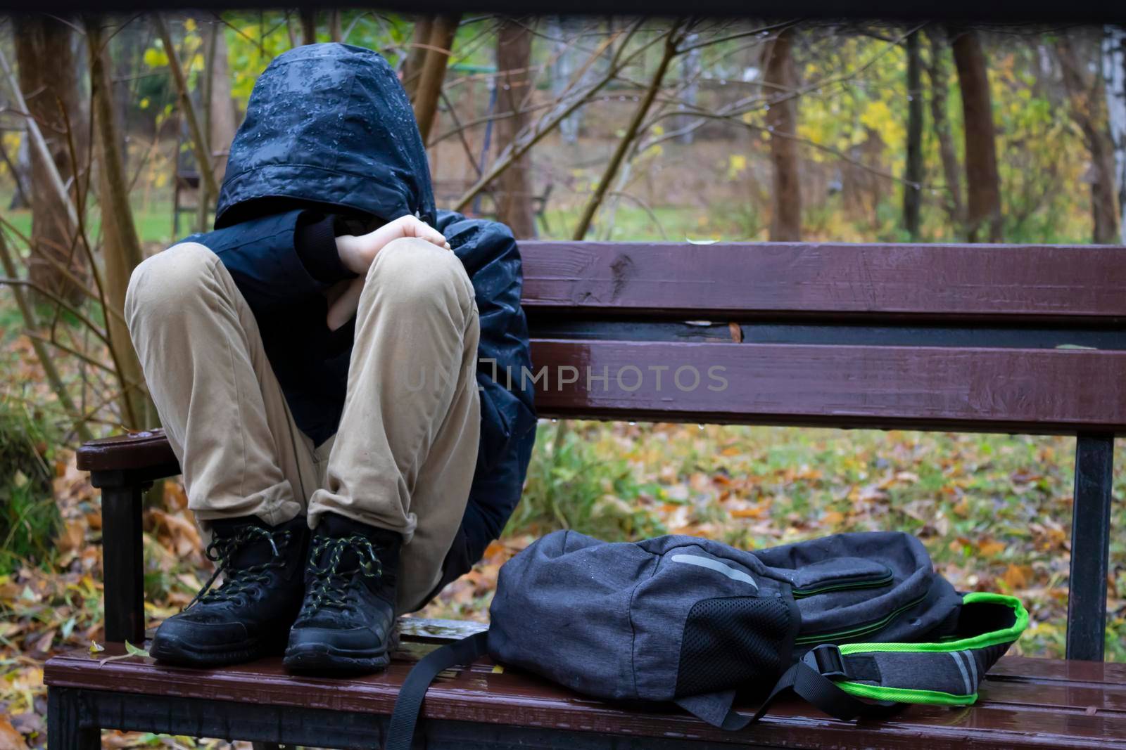 After school, a frustrated pupil in the park sits on a bench in an autumn park, bullying, problems with classmates.
