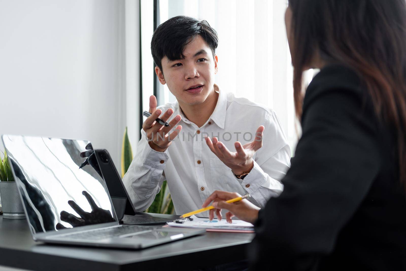 Young asian male mentor coach worker talking to female coworker teaching intern having business conversation with workmate, serious hindu manager helping colleague discussing new project in office
