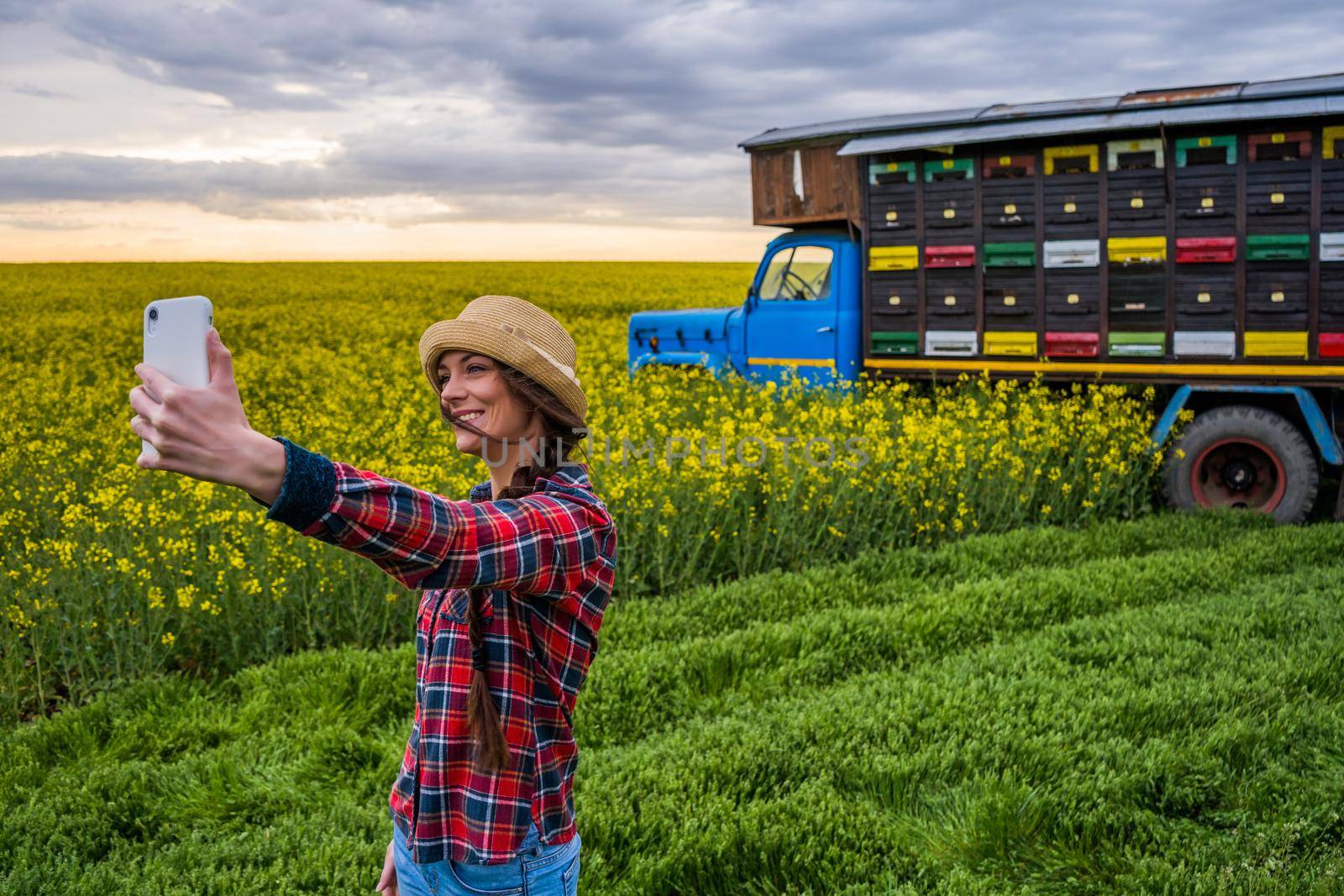 Proud female beekeeper is taking selfie in front of her truck with beehives.