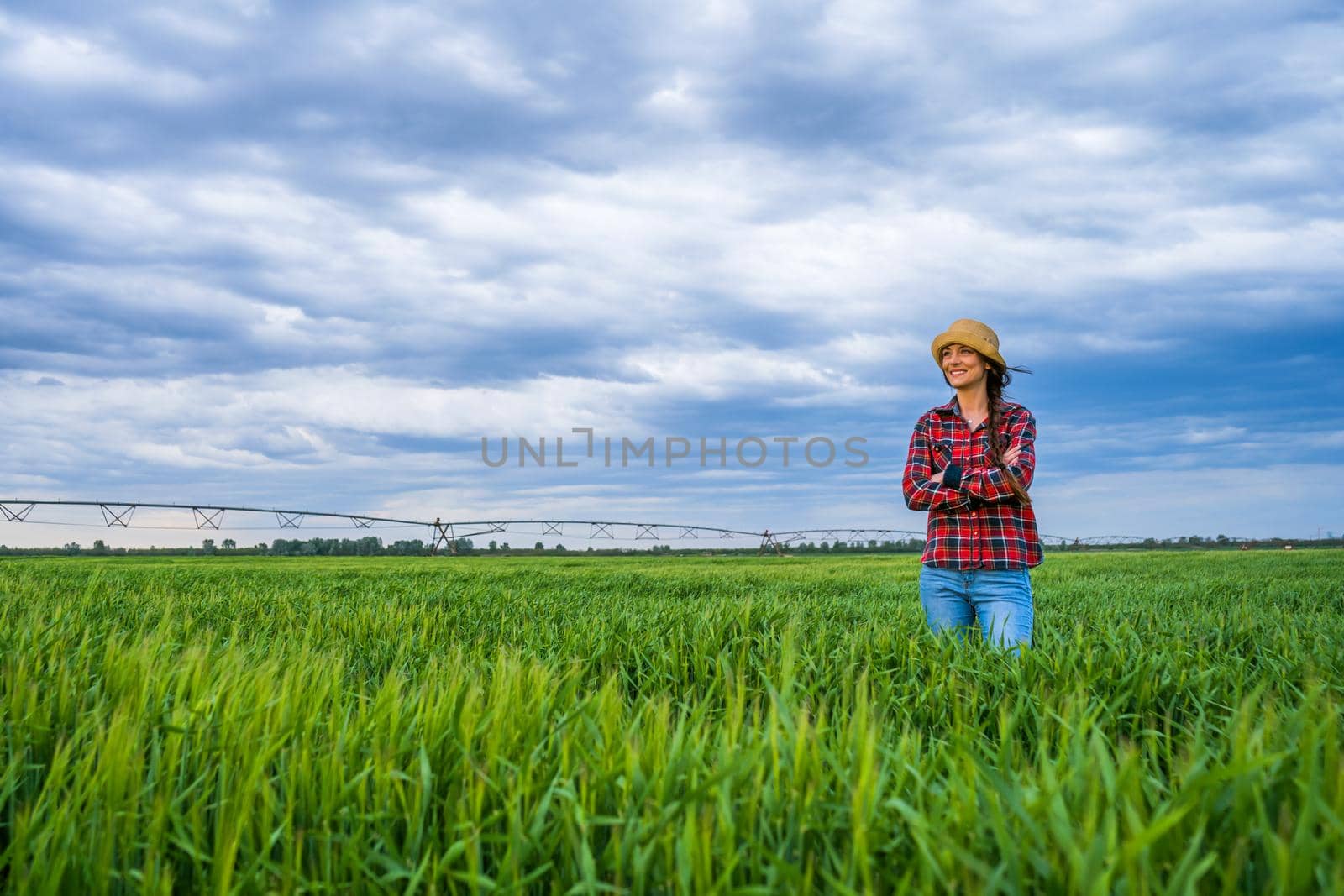 Proud female farmer is standing in her barley field and enjoying sunset.