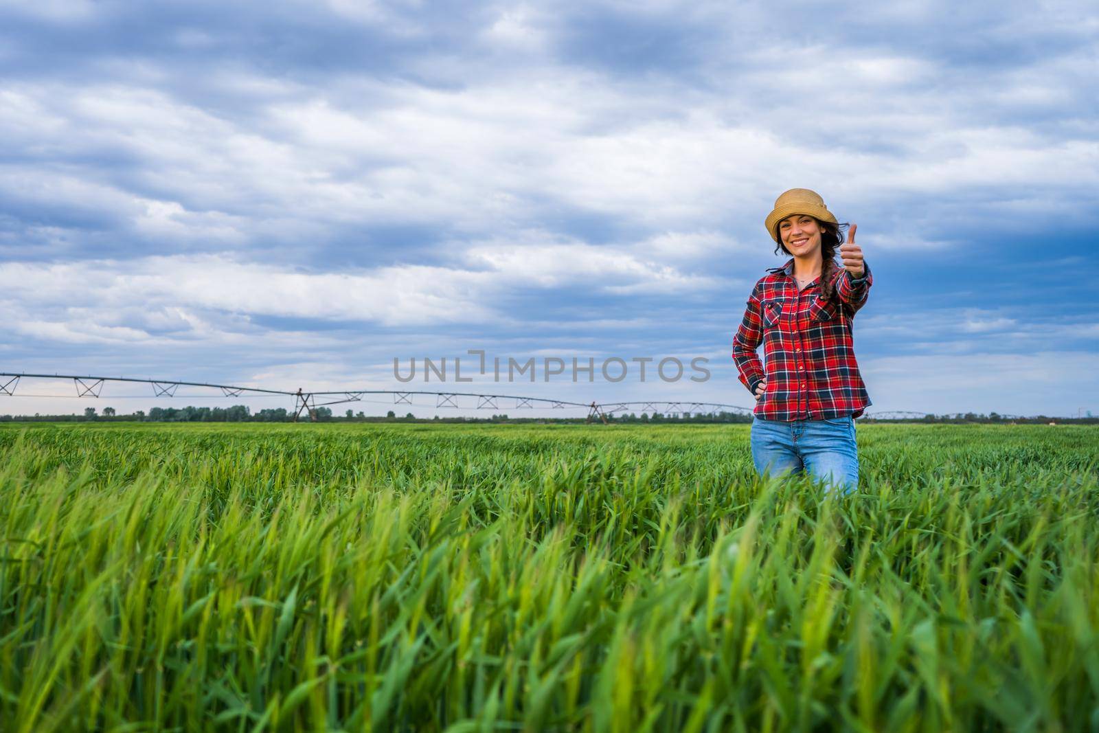 Proud female farmer is standing in her barley field and enjoying sunset.