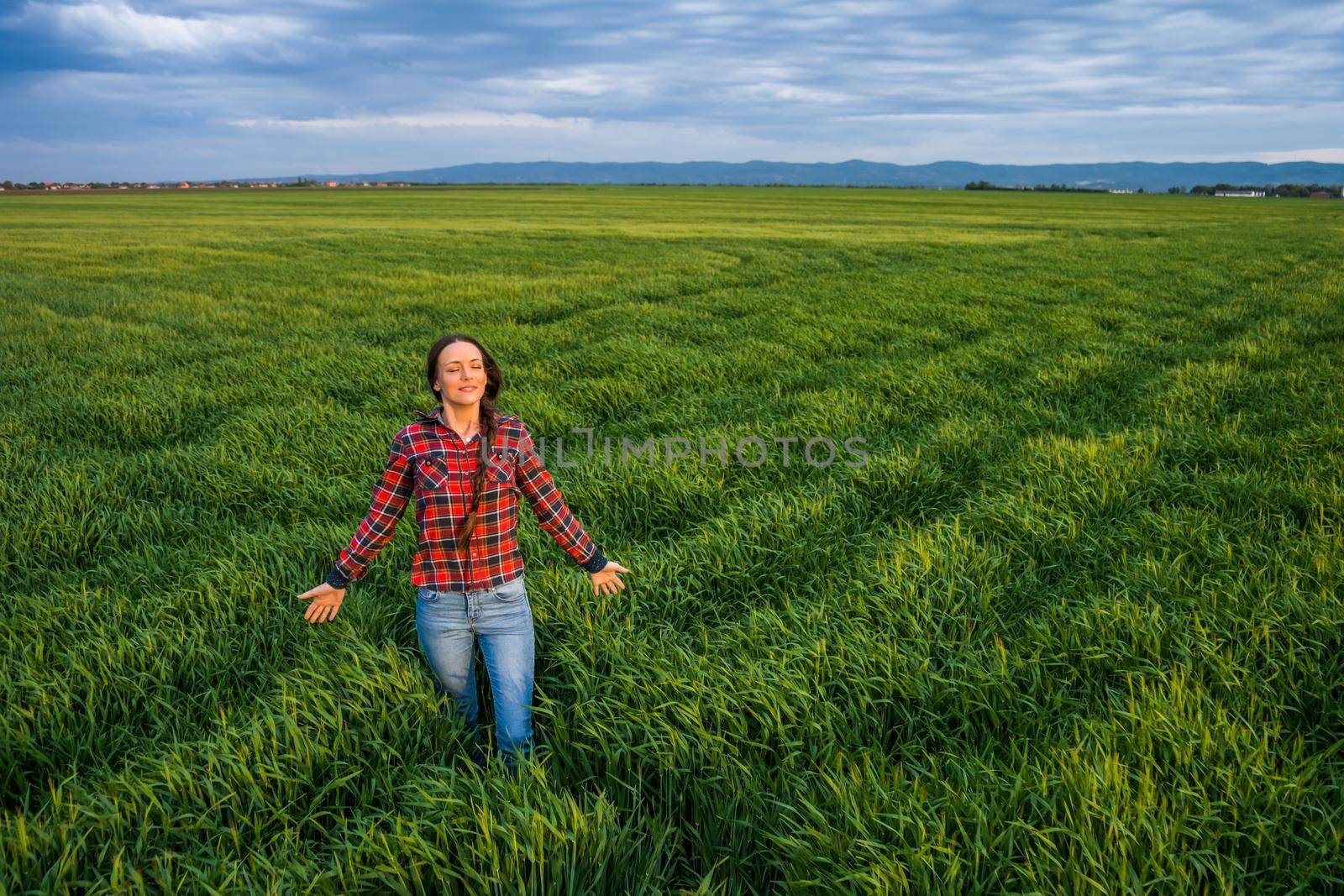 Proud female farmer is standing in her barley field and enjoying sunset.