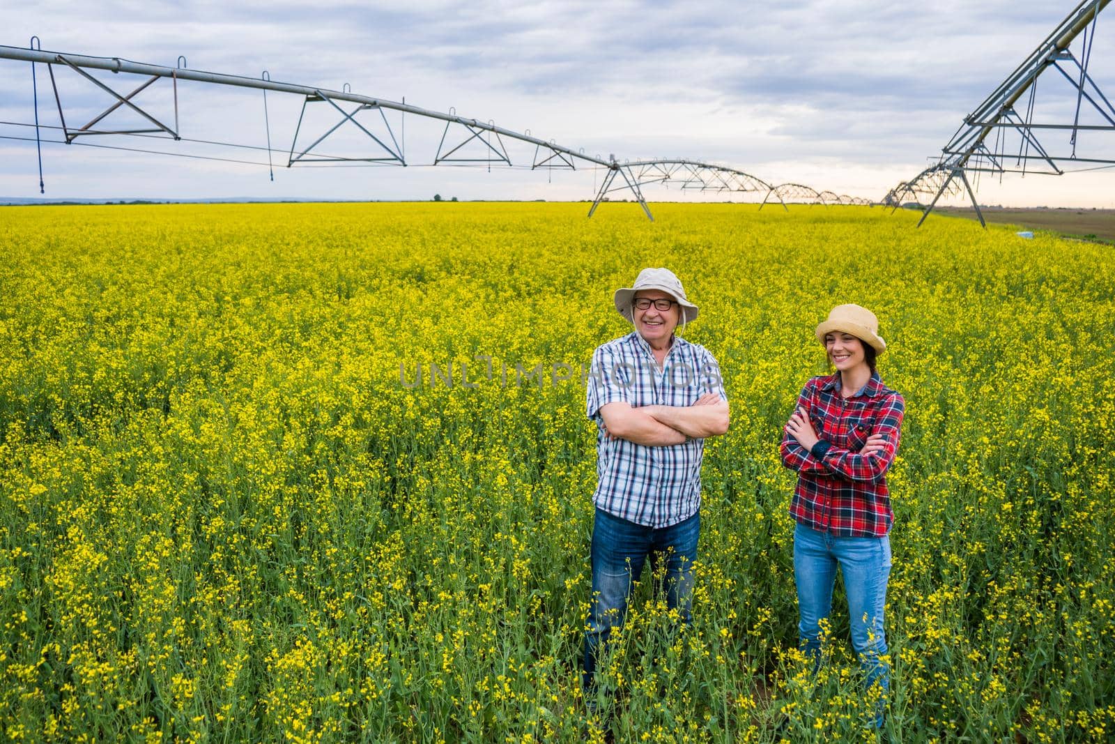 Proud two generations farmers are standing in their rapeseed field.