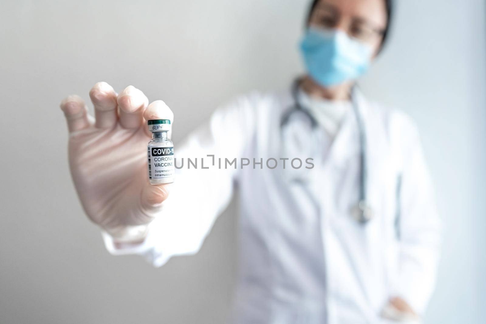 Medical woman or health worker in full protective kit show to the camera a vial of Covid-19 vaccine in selective focus holding it in her hand with gloves. Concept of global pandemic vaccination by robbyfontanesi