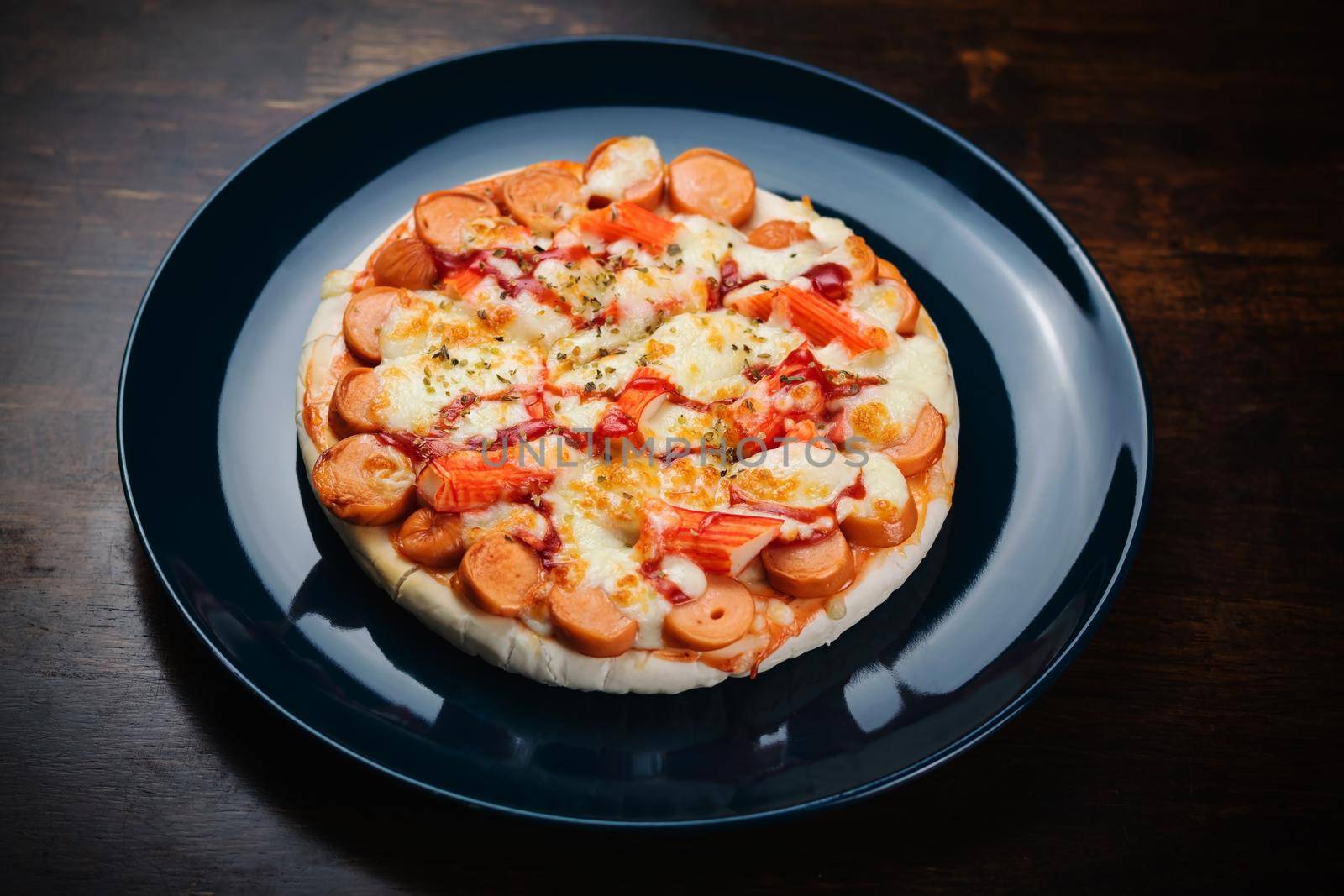 Pizza, sausage and crab sticks in a ceramic plate on a wooden table.