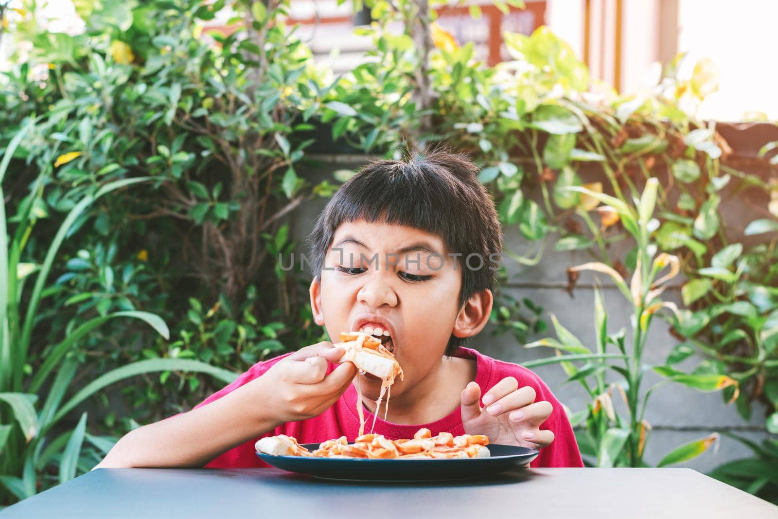 Asian cute boy in red shirt happily sitting eating pizza.