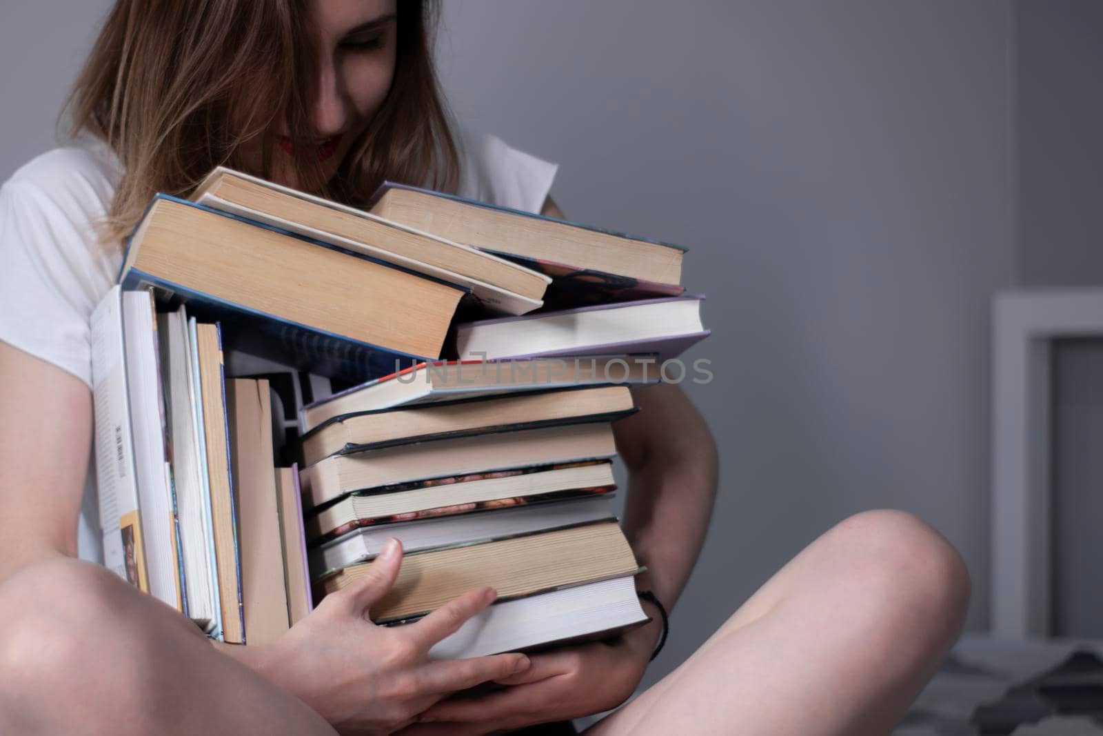 happy beautiful slim girl holds a lot of different books in her hands. Homeschooling. Studying in quarantine. Reading is helpful - horizontal photo