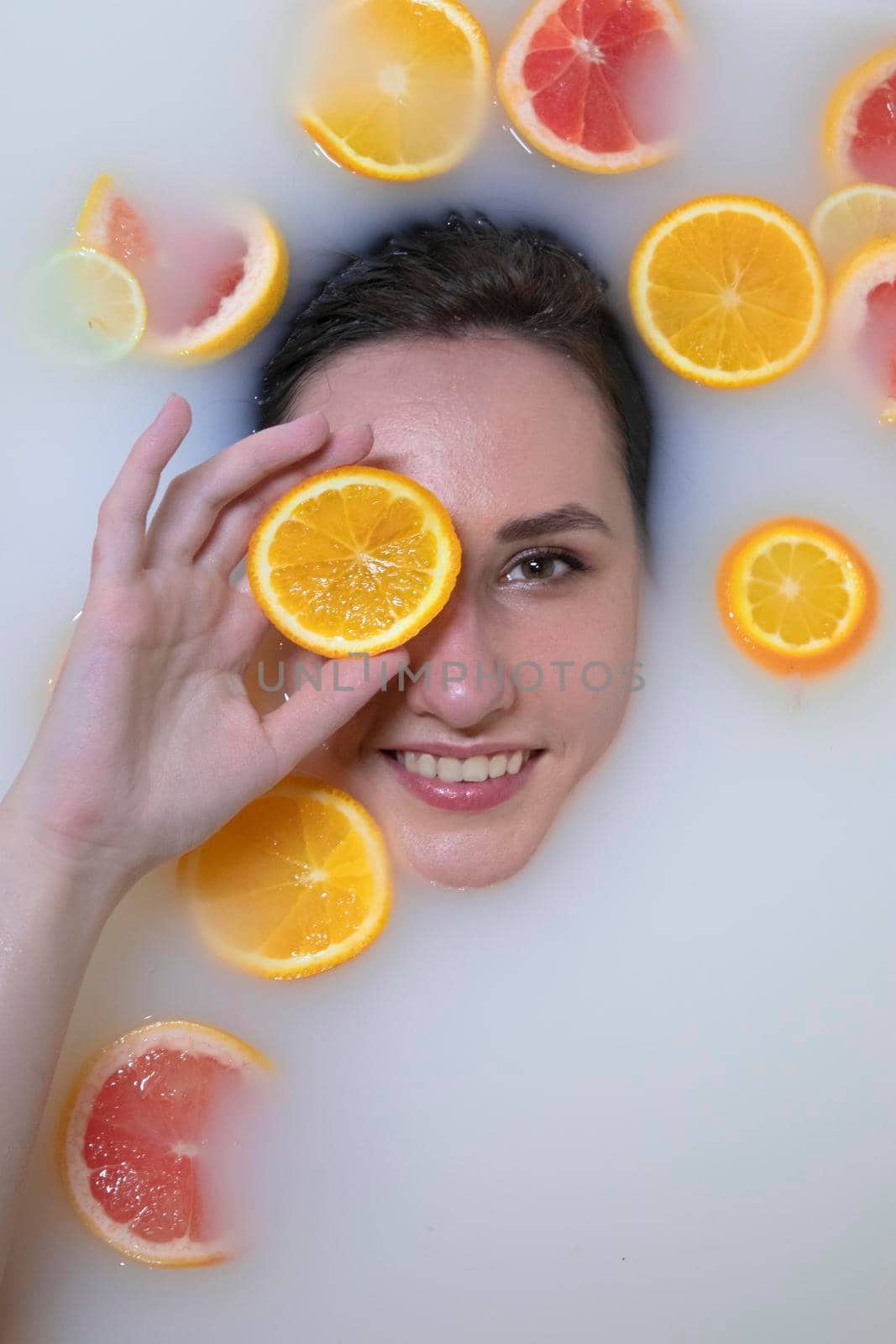 Woman portrait in milk bath with oranges, lemons and grapefruits. Fashion model, spa and skin care concept. by oliavesna