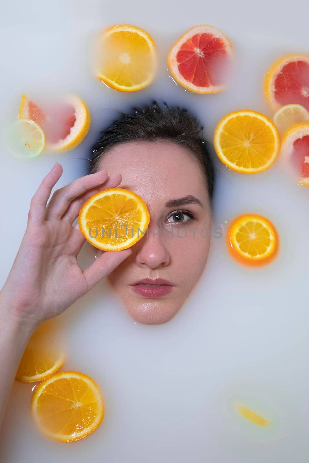 Woman portrait in milk bath with oranges, lemons and grapefruits. Fashion model, spa and skin care concept. by oliavesna