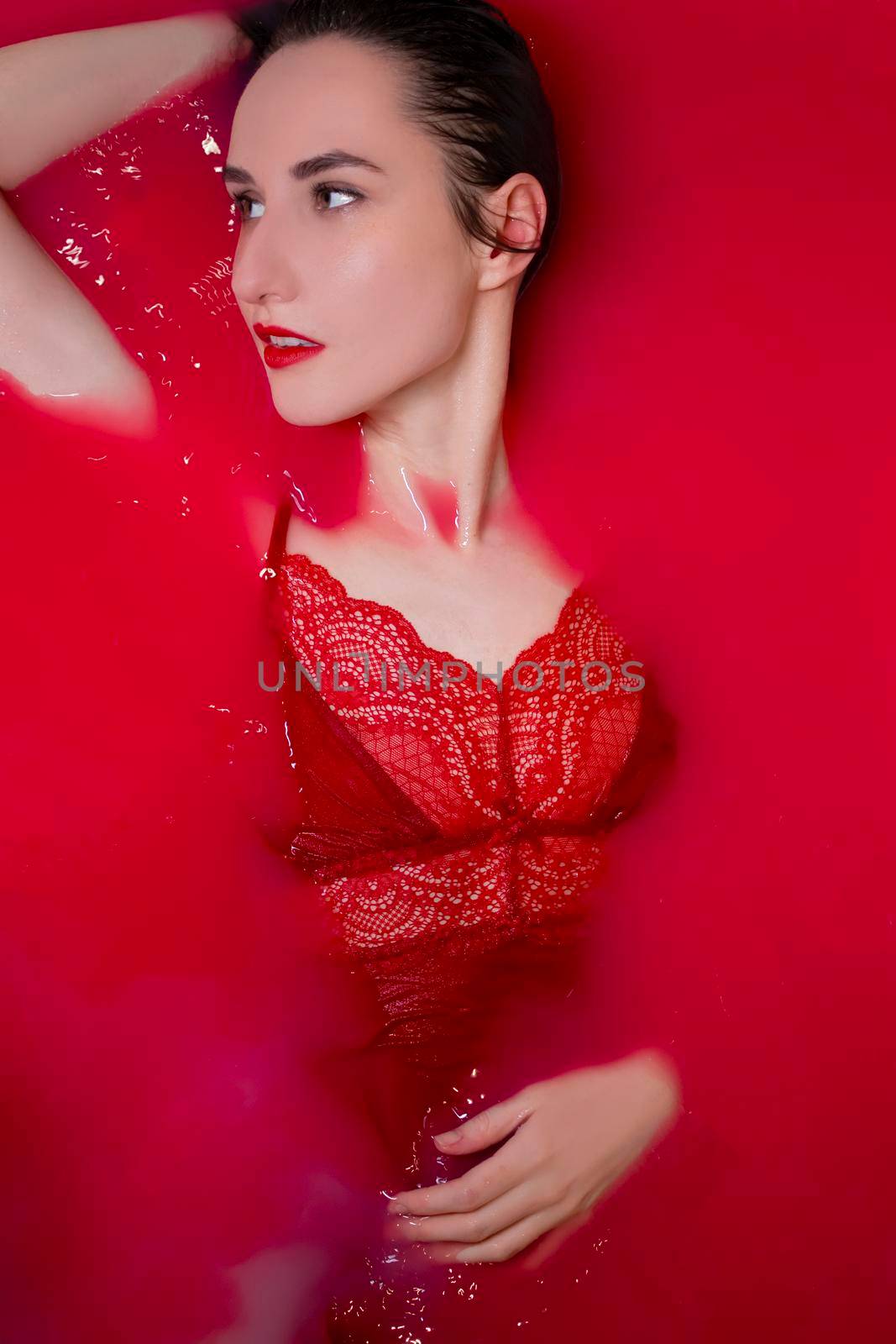 portrait of a beautiful brunette in red lingerie in red water. horror films. Photoshoot in the bathroom. copy space.