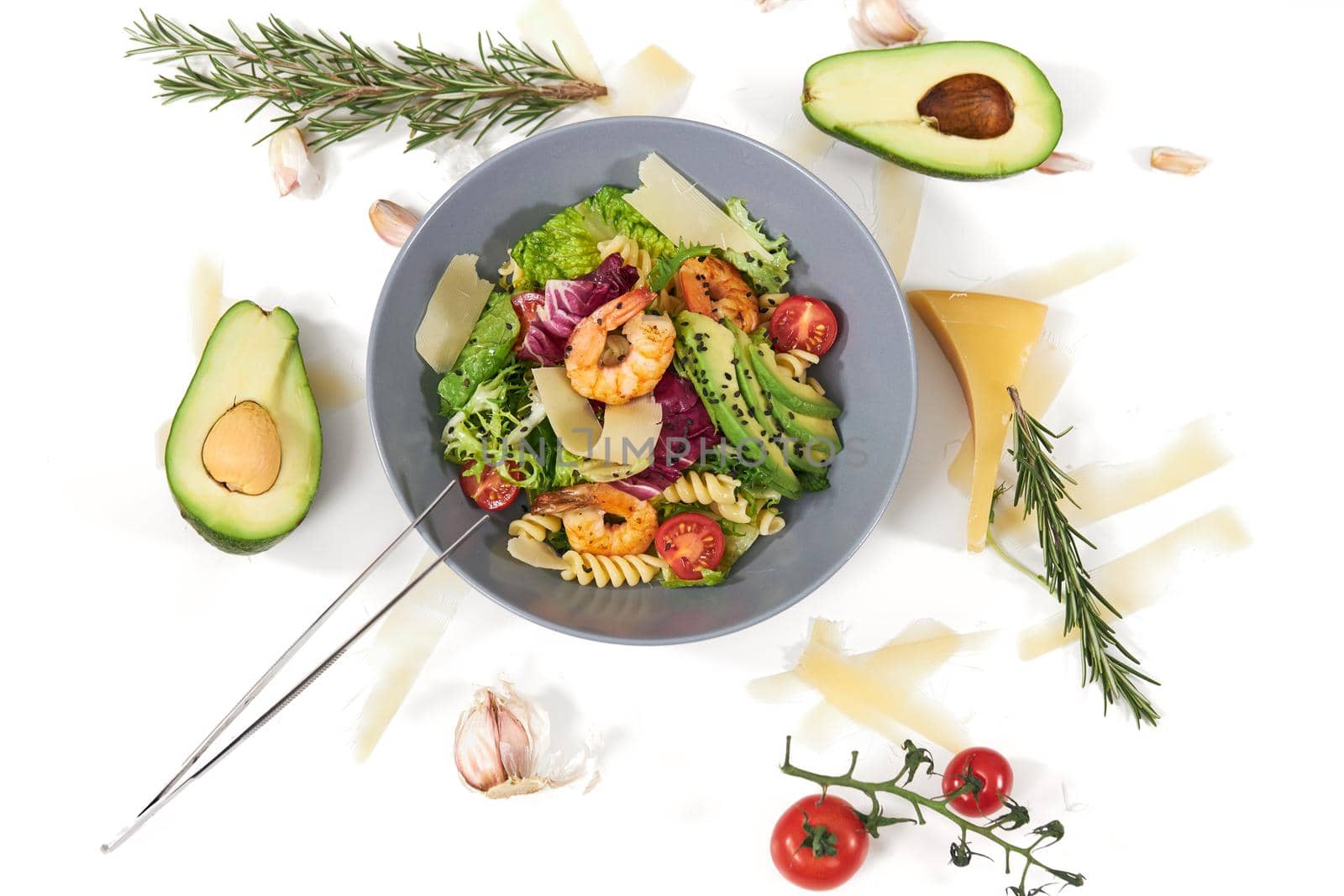 Top view of modern blue bowl with pasta,seafood,avocado,tomatoes and fresh leaf greens on white background. Concept of beautiful composition with vegetables and tasty cheese and herbs. 