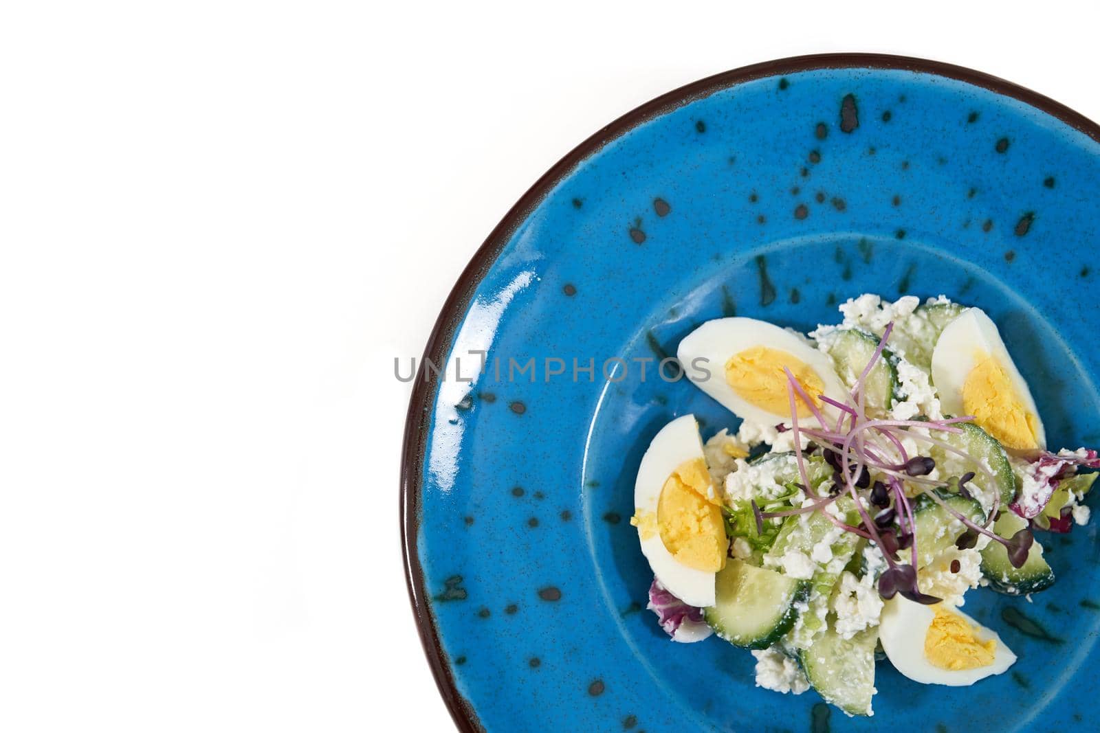 Top view close up of modern beautiful blue plate with tasty salad eggs,cucumber,cottage cheese and fresh greens. Concept of tasty and healthy salad for maintain body weight.