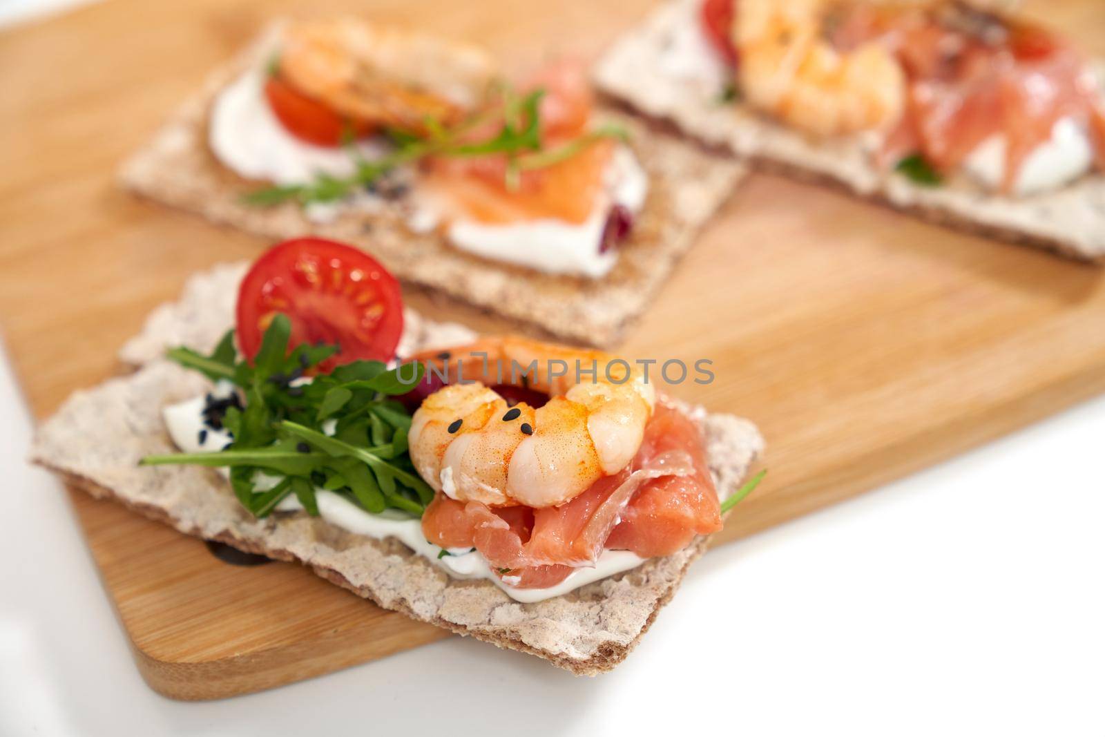 Close up of appetizing sandwich of diet breads with shrimp, salmon and tomatoes,arugula on wooden board. Concept of delicious snacks with seafoods in restaurant or home. 