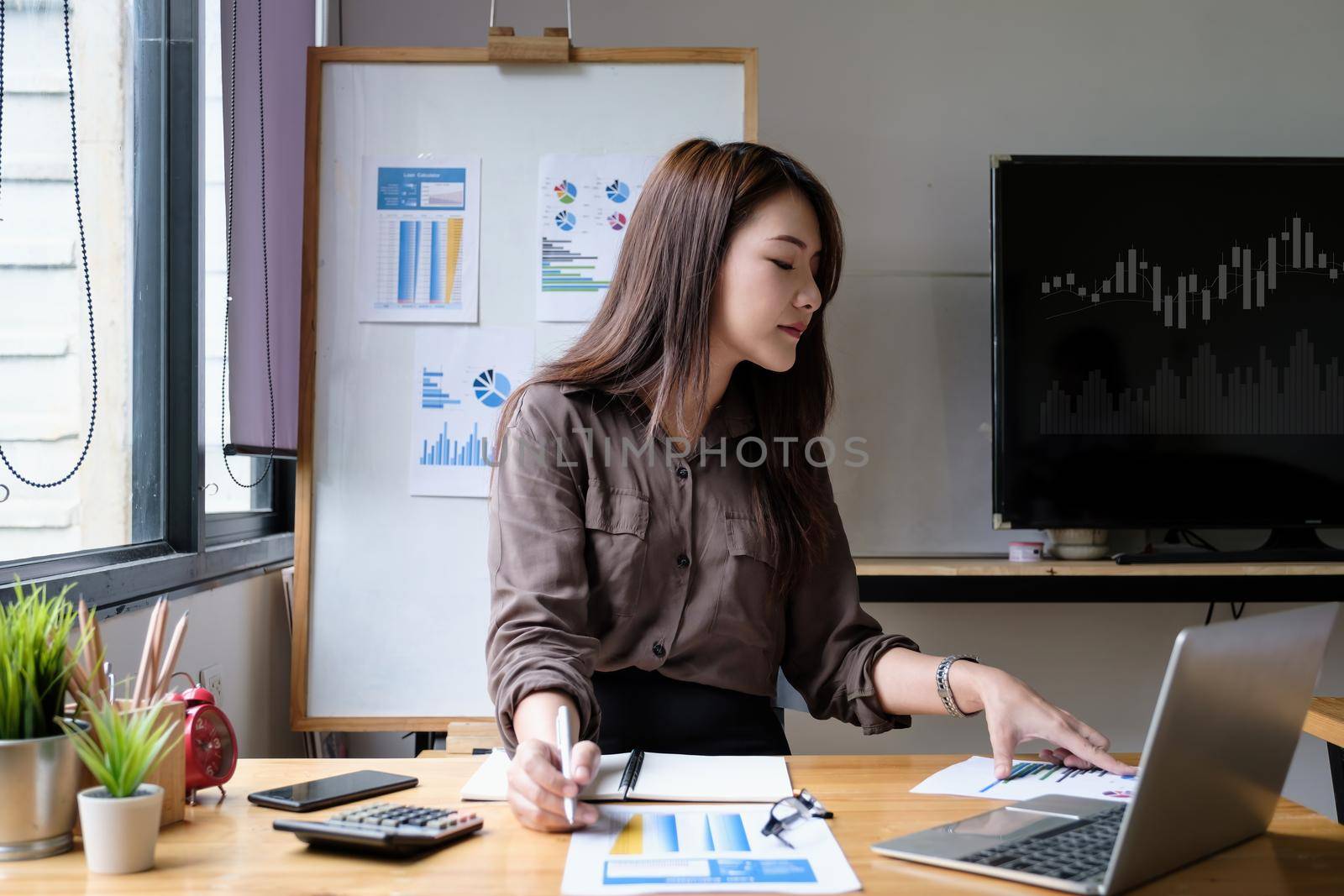 Close up of businesswoman or accountant hand holding pen working on calculator to calculate business data, accountancy document and laptop computer at office, business finance concept. by itchaznong