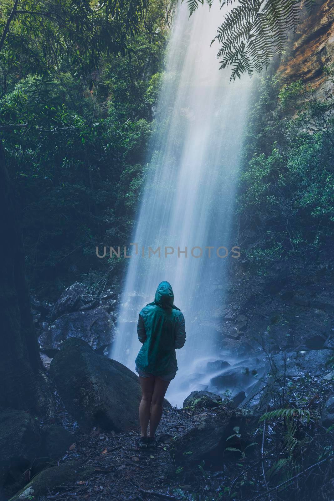 Woman hiker standing below a waterfall after rain by lovleah