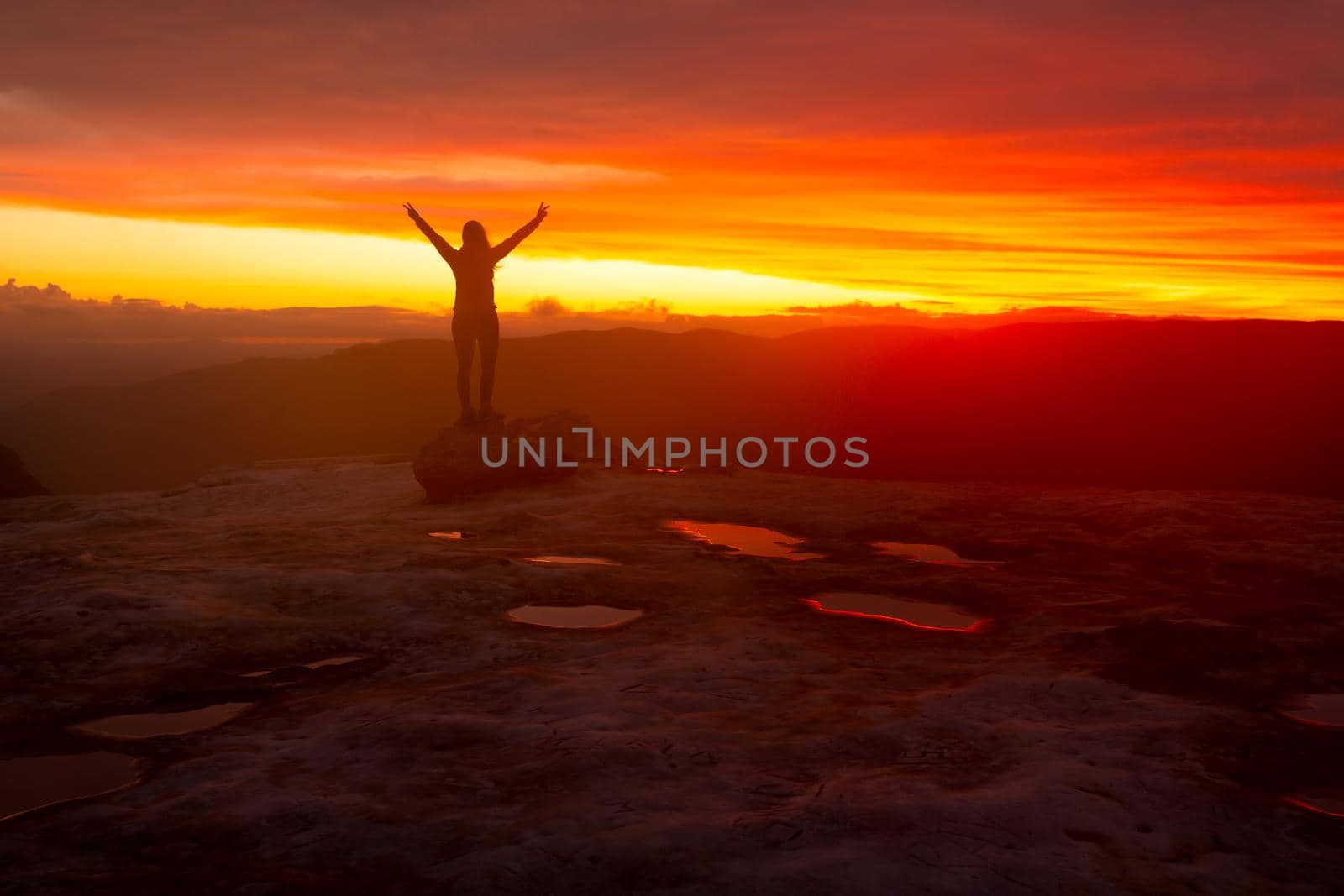 Woman looking out over mountains, her silhouette against red sunset sky