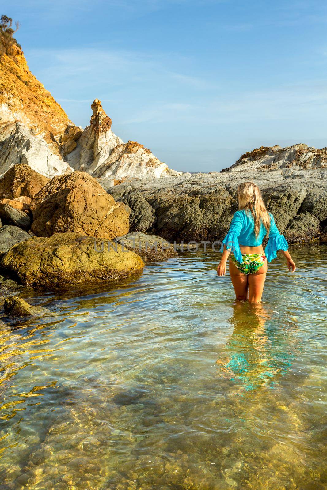 Woman wading into natural rock pool in early morning light.  She is wearing a swimming costume and bright blue midriff top.  Recreation, leisure, travel or tourism