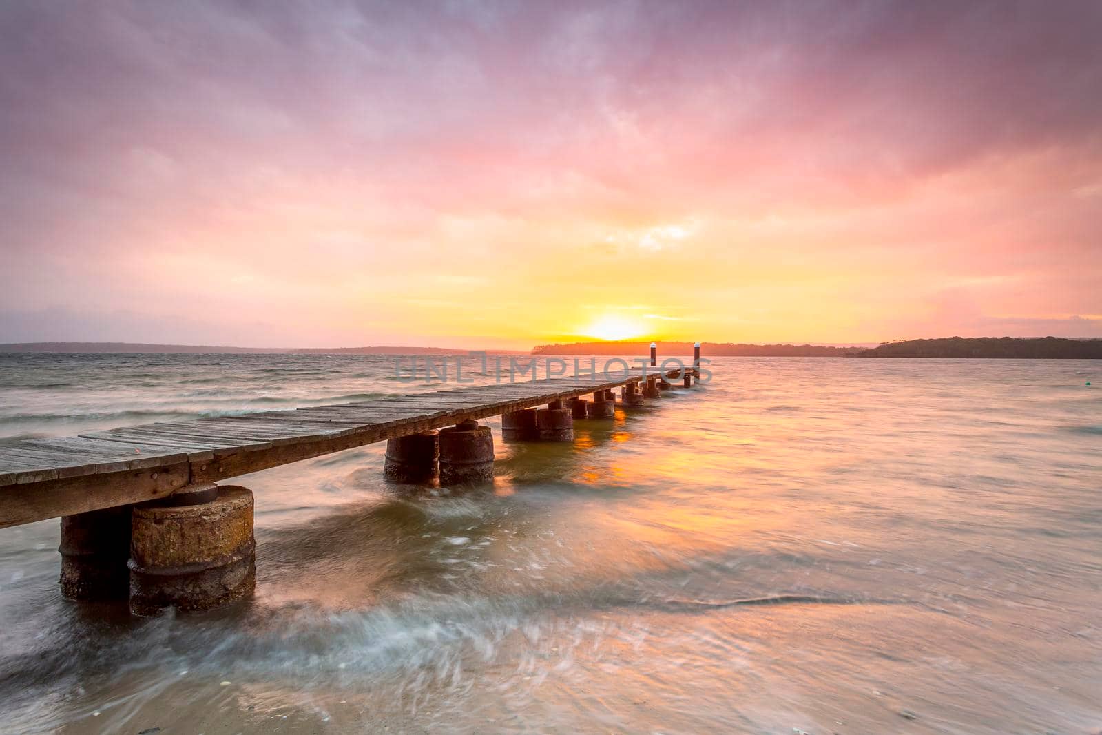 Beautiful sunset of lovely colours and a timber plank jetty on concrete pylons on waters whipped up by winds