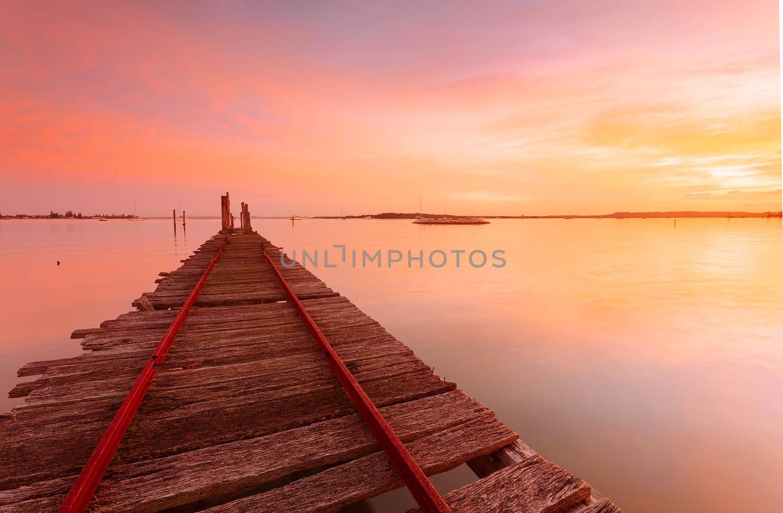 Sunrise sky and reflections at the old rustic timber  oyster jetty weathered timber planks with rusty nails protuding