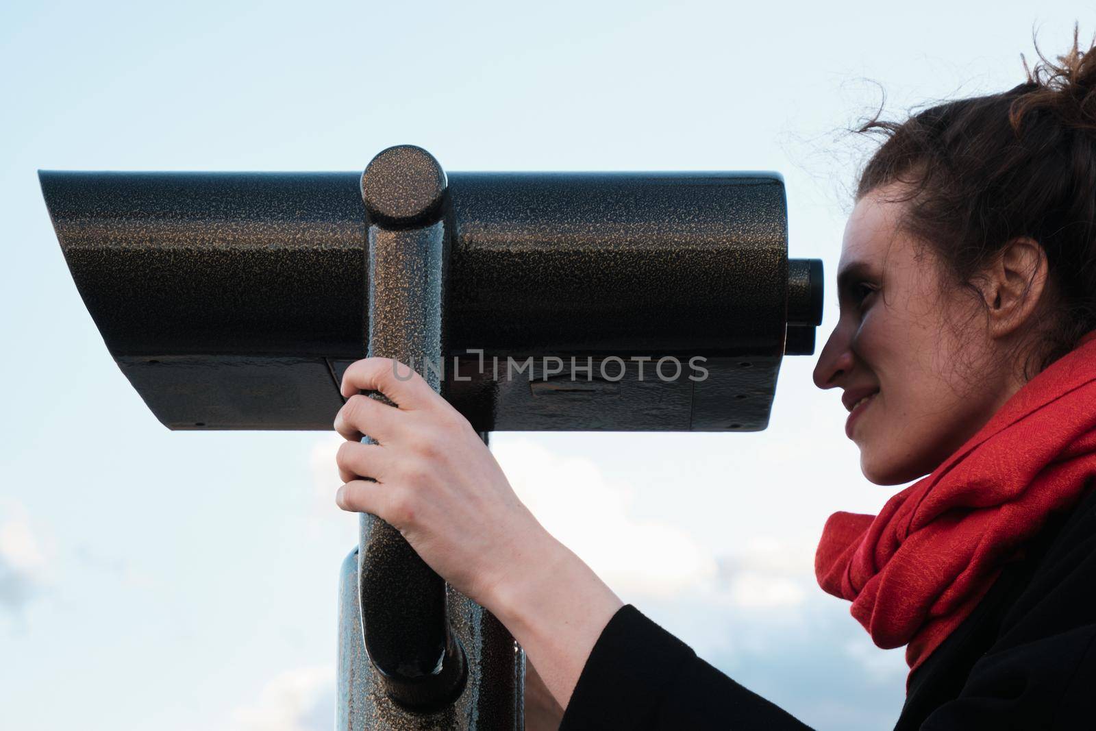 A young girl looks through a large city binoculars. City landmarks