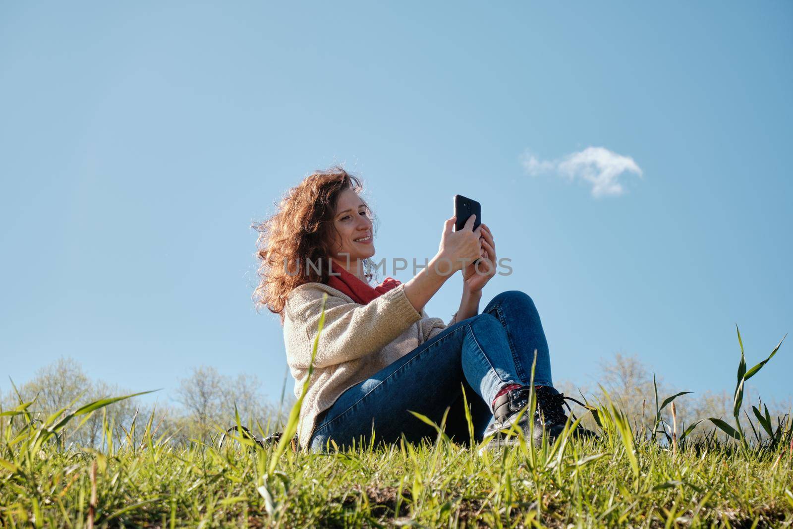 Young girl with a phone in her hands, green grass and blue sky