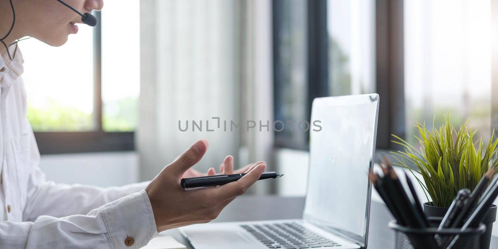 Focused young businessman manager wearing headset with microphone, involved in distant online meeting with colleagues or partners, discussing working issues using video call computer application. by wichayada