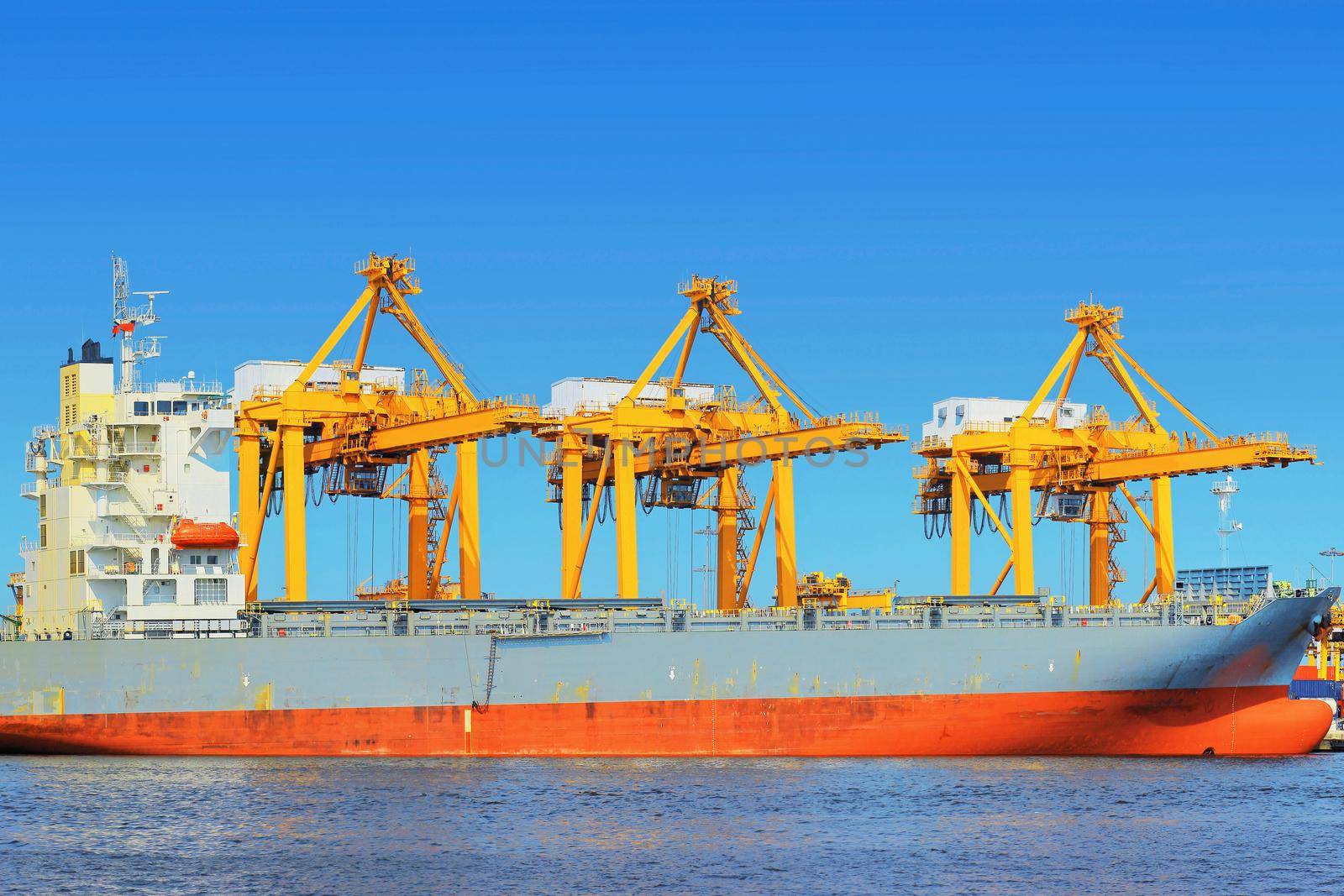 Container Cargo freight ship with working crane bridge in shipyard.