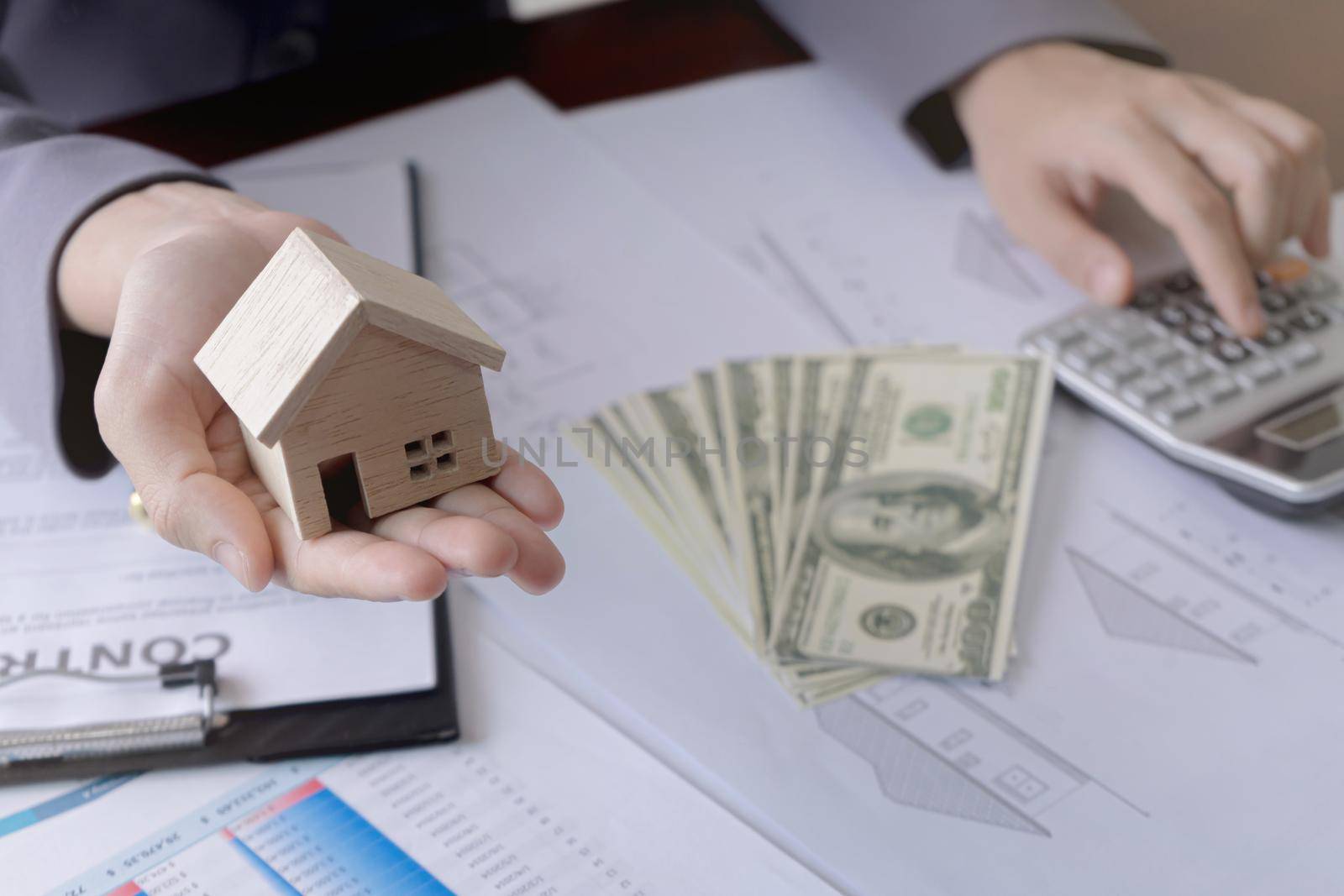 Real estate agent showing a miniature model house to the customer and using calculator. Concept for real estate, moving home or renting property.
