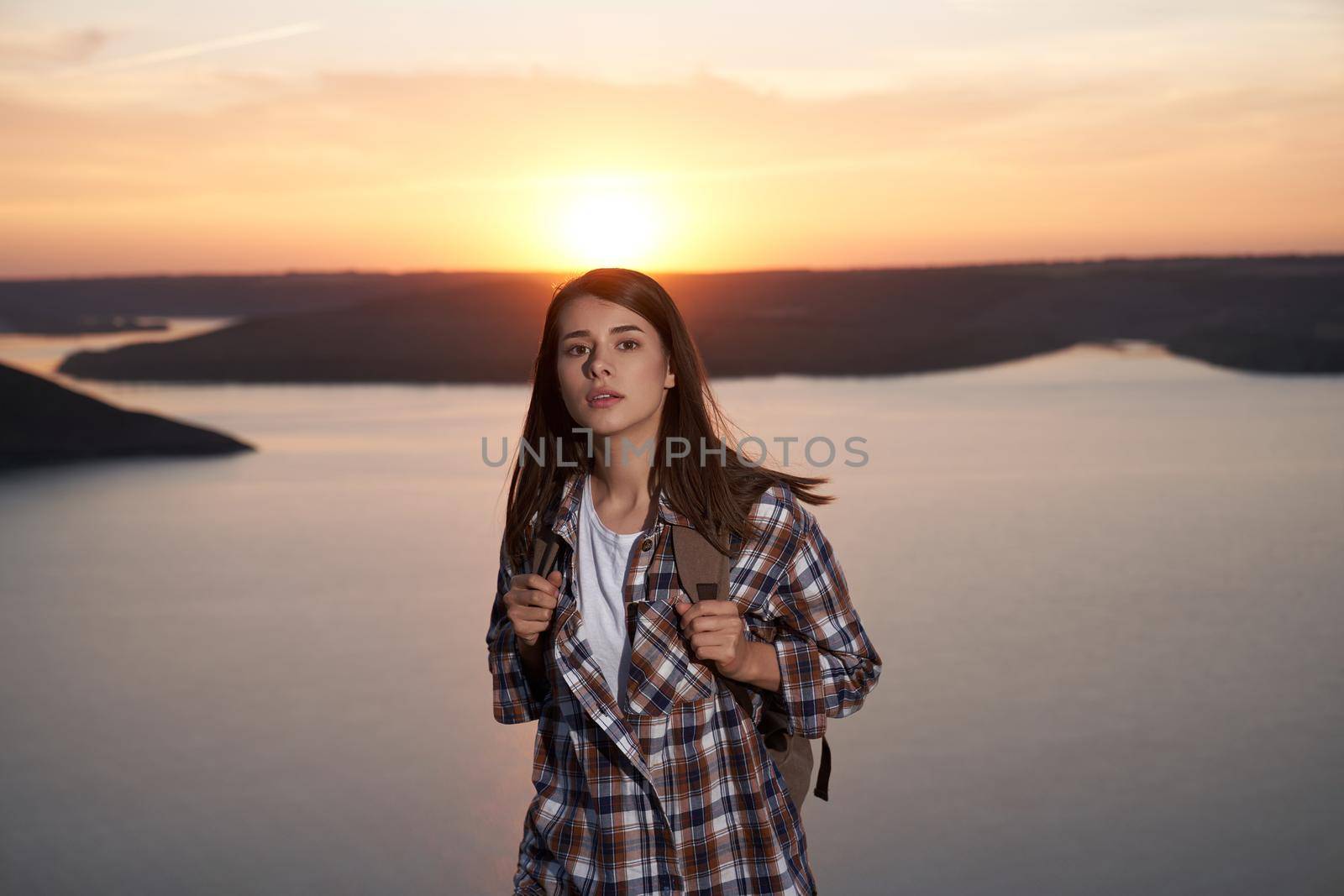 Adorable female tourist with backpack posing during amazing sunset at Bakota bay. Happy woman with brown hair walking outdoors during evening time.