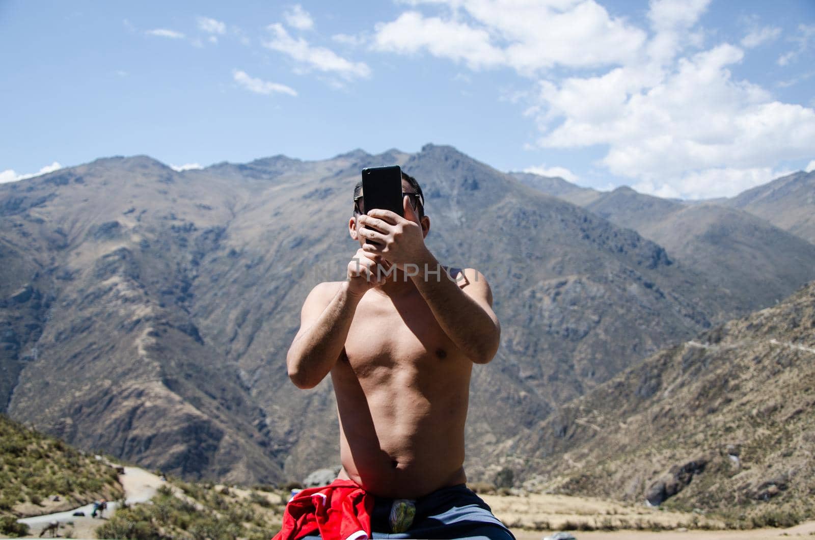 Young man using a smartphone. Holding mobile smart phone, without polo, with black sunglasses on the background of mountain nature.