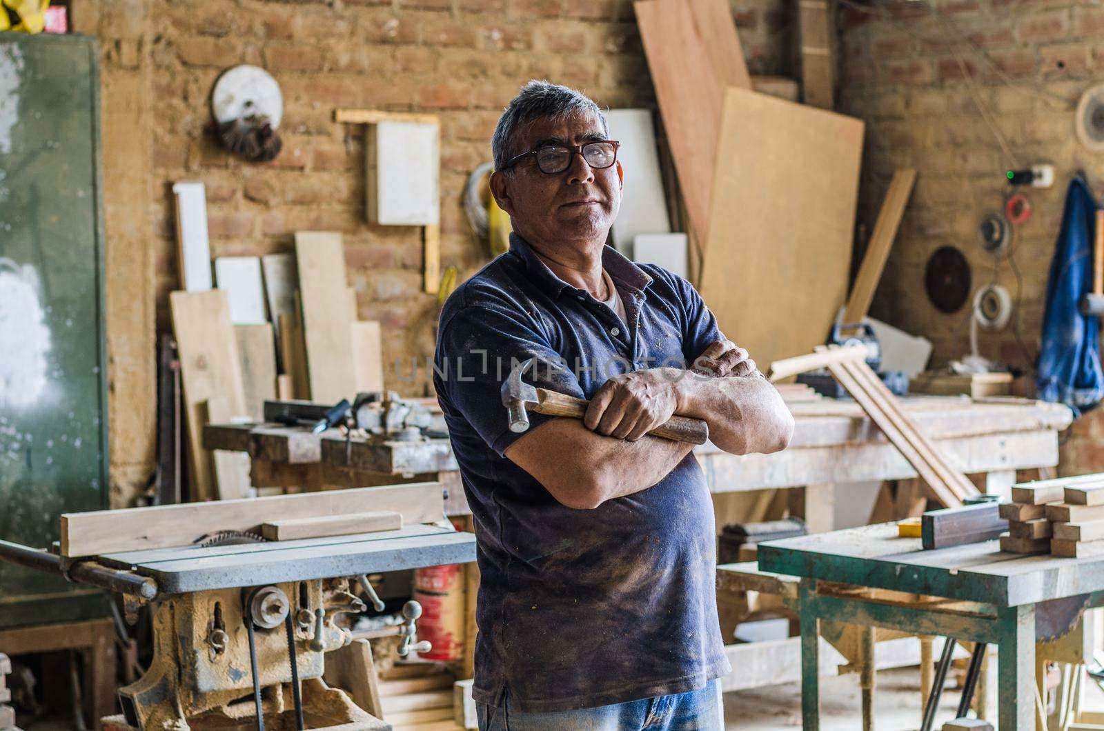 Portrait of senior carpenter. Standing in his workshop and looking at camera.