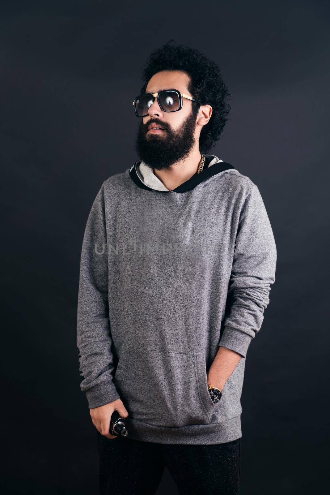 Thoughtful bearded young man with gray sweater and sunglasses. Man holding a mod. Black background.