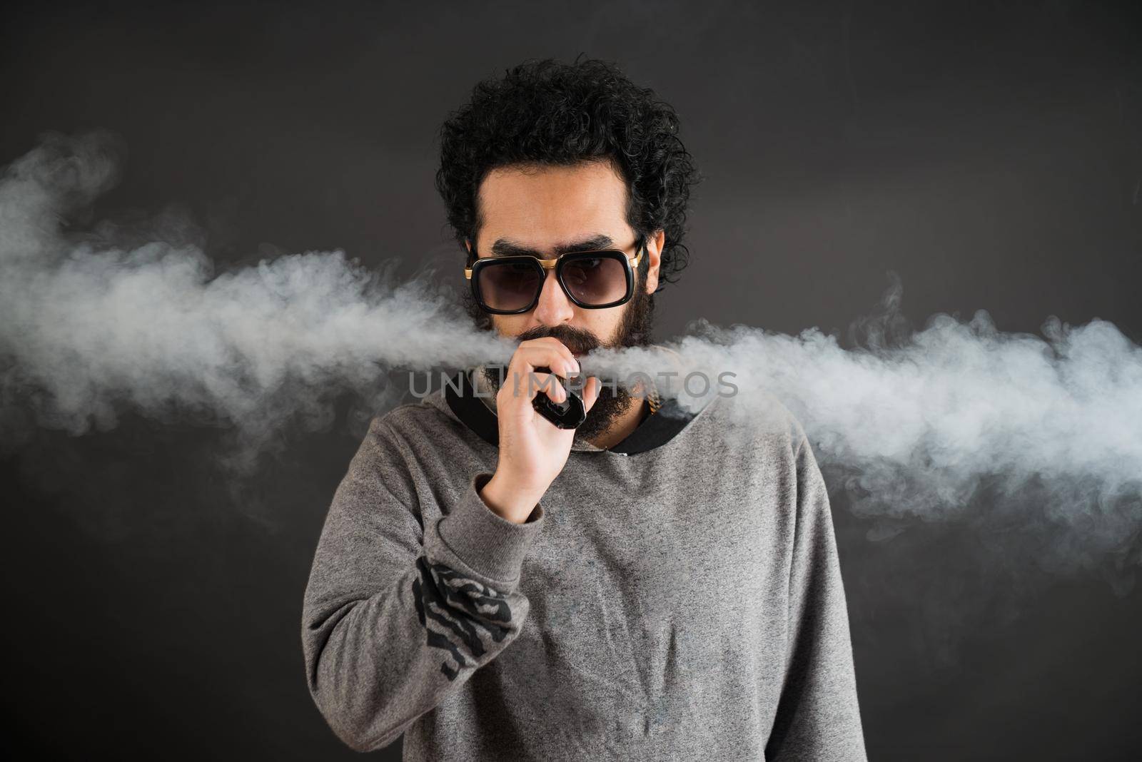 Vaping man holding a mod. A cloud of vapor. Black background. Vaping an electronic cigarette with a lot of smoke. Vape concept