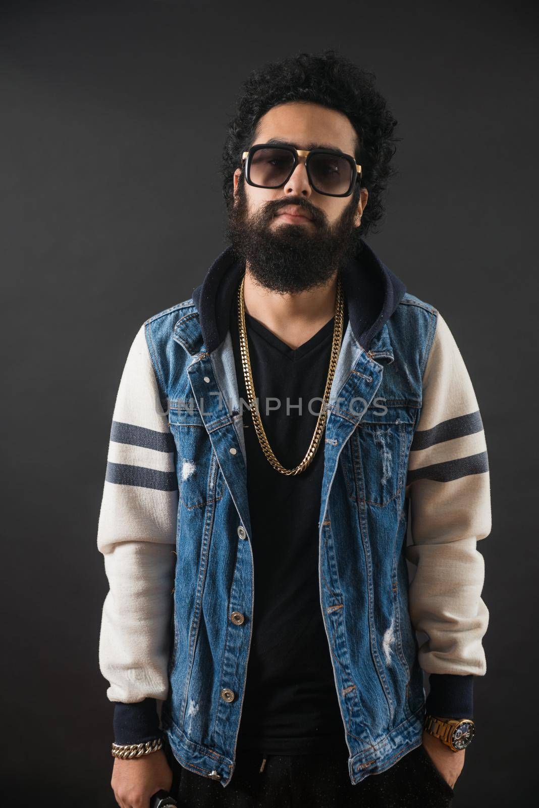 Thoughtful bearded young man with gold chain and jeans sweater and sunglasses. Man holding a mod.